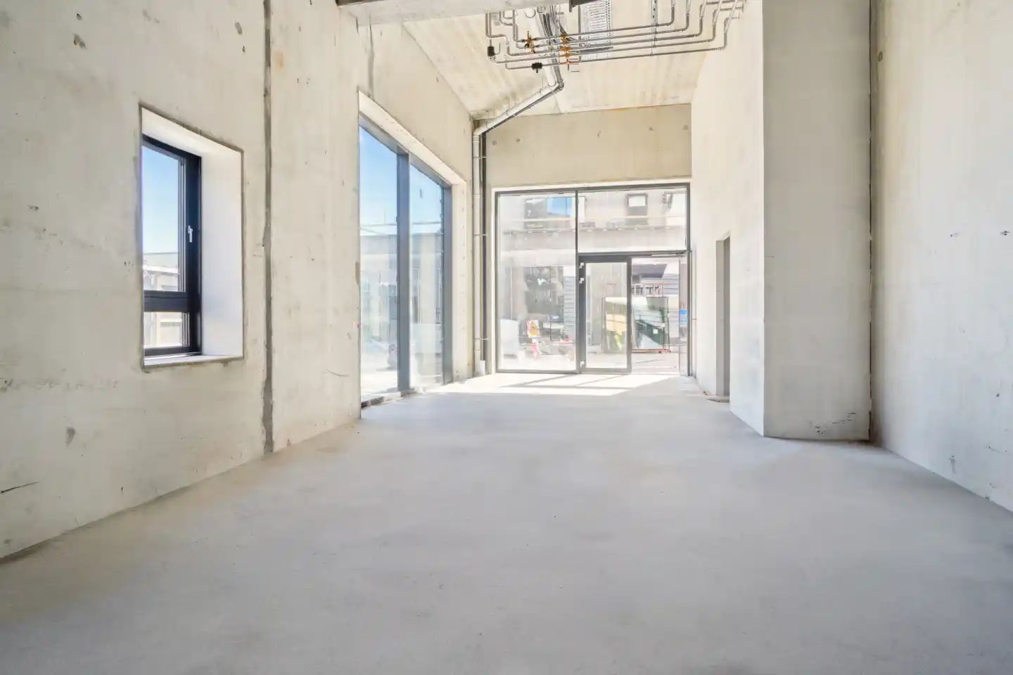Et ubeboet lokale med store vinduer og åbne døre til gaden med bygningsmaterialer udenfor