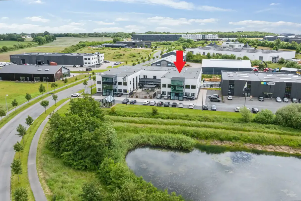 Et moderne firmabygning med parkeringsplads og have samt sø i forgrunden