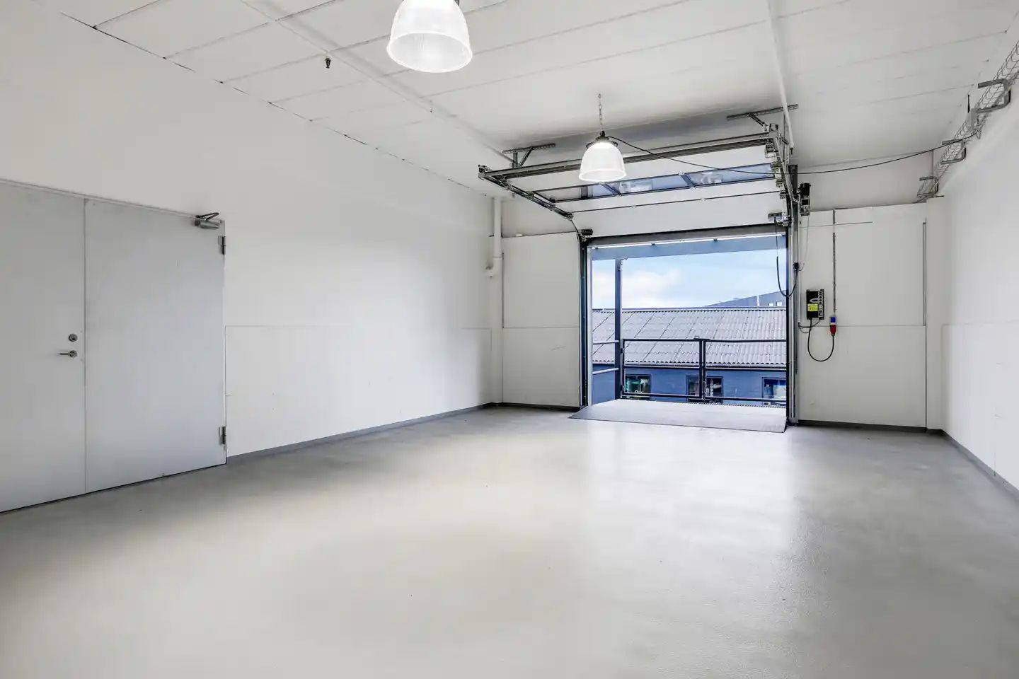 En stor, lys garage med åbne hvide vægge, gulv og loft samt trægulv og hvide døre og loftslamper