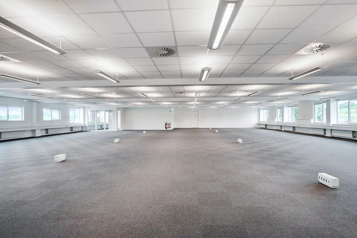 Kontorområde med lyse hvide lofter og gulve samt flere vinduer og to brandblusser