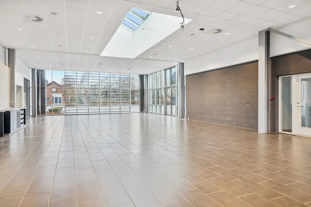 Store rum med lyse lofter og en stor vinduesvæg mod gården. Gulvet er lavet af lysegrå og brun belægning.