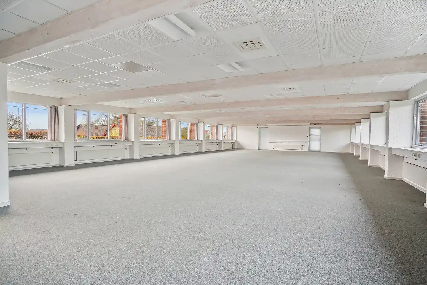 Rummelig og mørk kontorlokaler med hvide lofter og gulve samt flere vinduer mod gårdsplads og træer