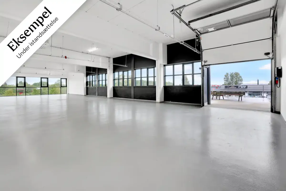 Lagerdelen har adgang via port og rampe, og gulvet er blankt og moderne. Væggene er hvide med store vinduer og lysearme. Der