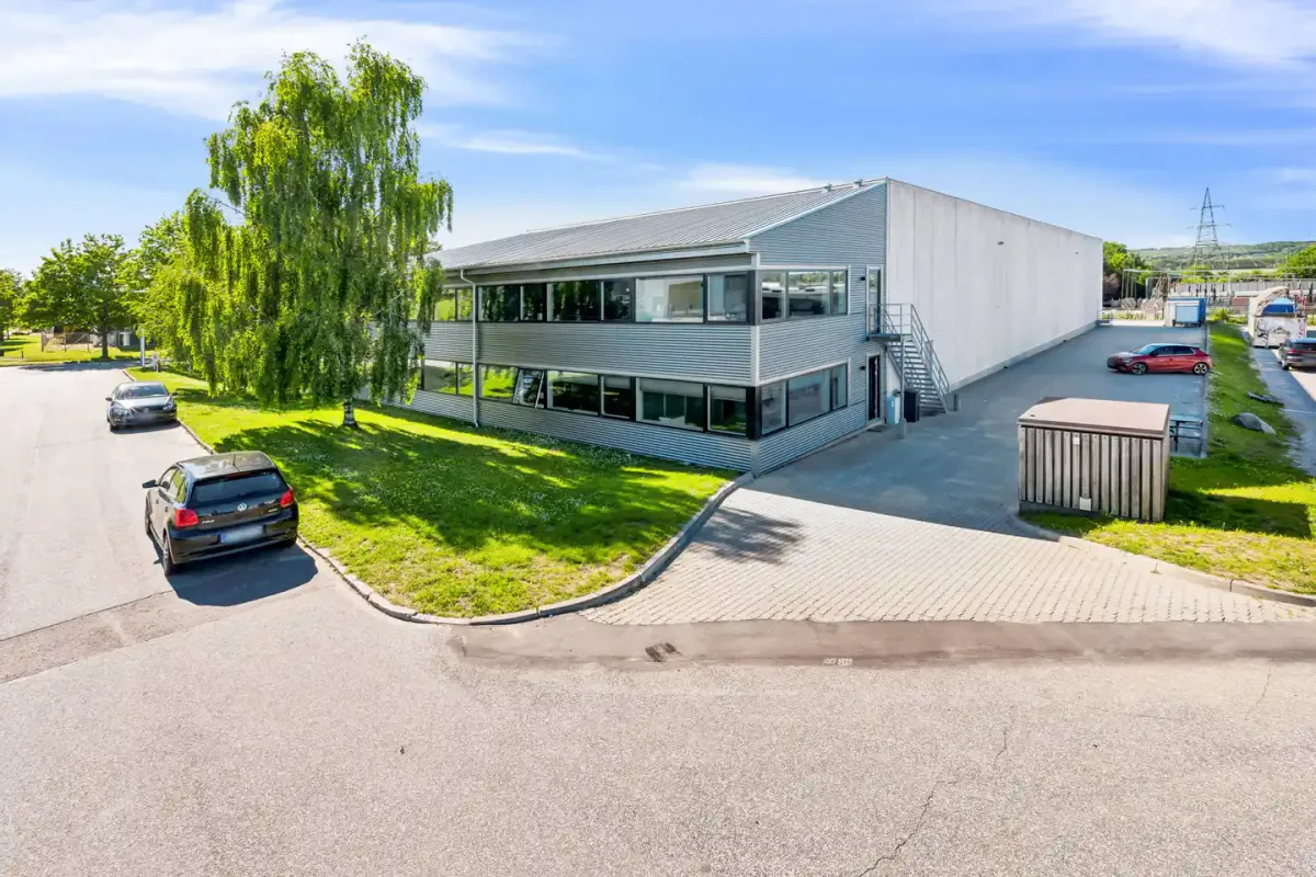 Et moderne kontorbygning med stort parkeringsområde, flere biler parkeret og smukke grønne områder.