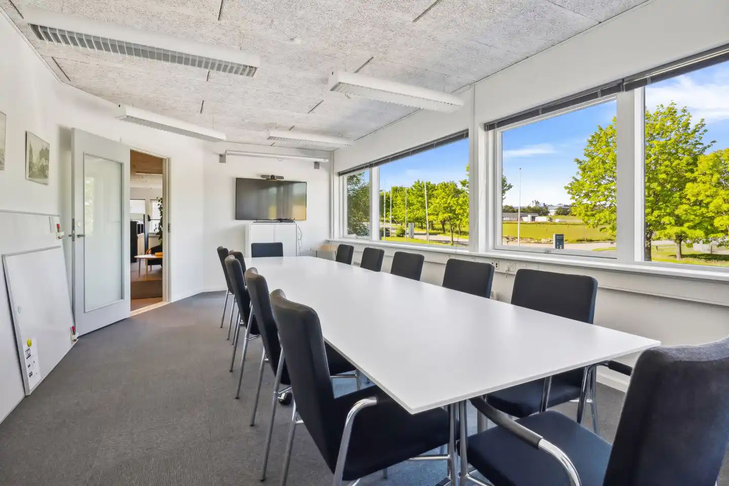 En stor mødesal med lyse hvide vægge, gulv og loft samt en lang mødebord og flere møbler og vinduer