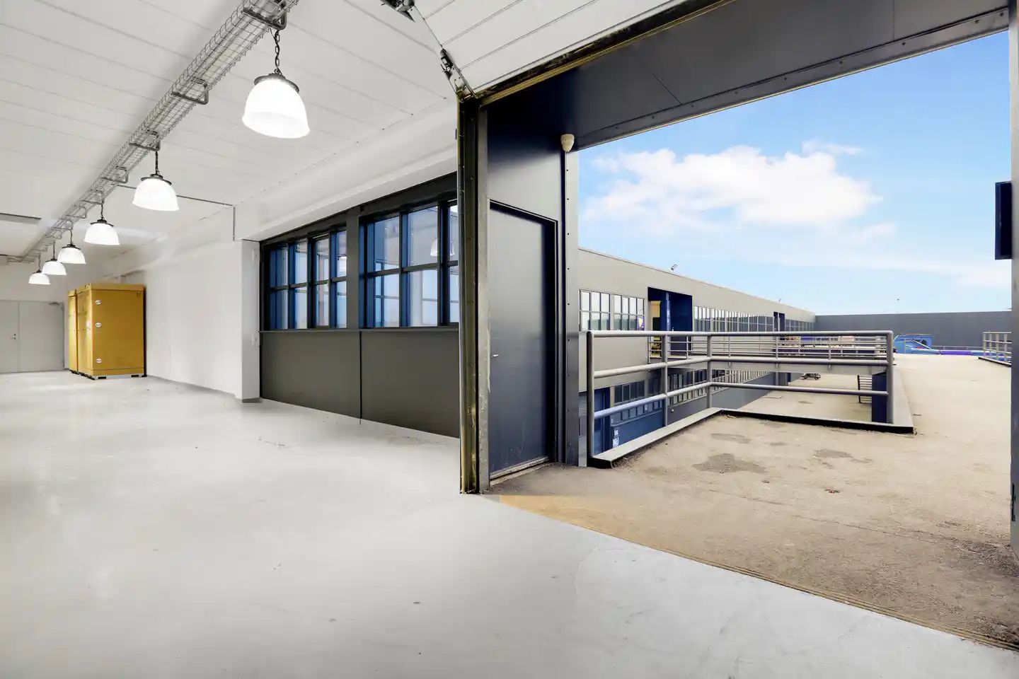 Vareadgang og vagtrum i et lager med åben dør og lysekroner samt lyse skyer i baggrunden