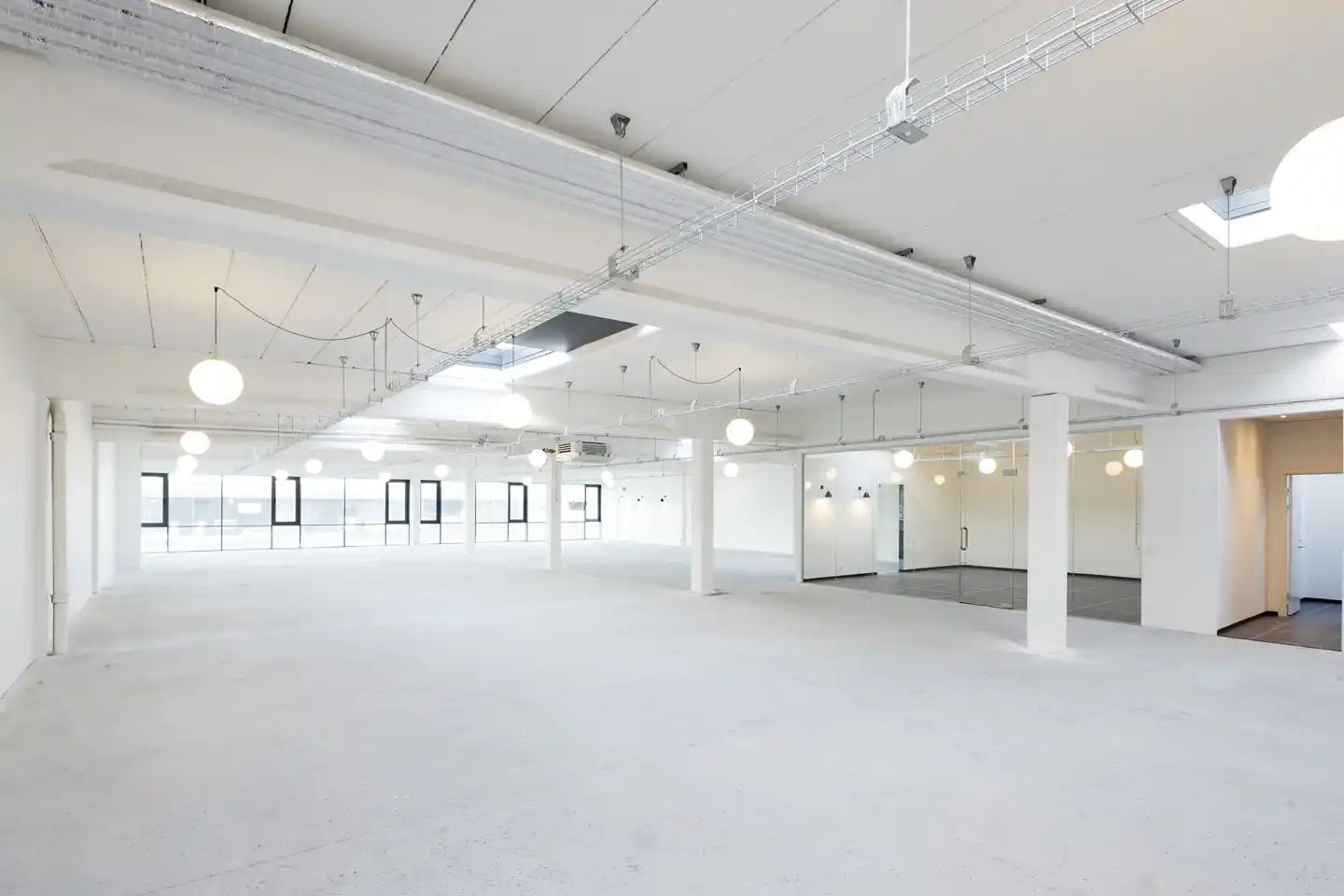 En stor, lys og åben industrilokal med hvide vægge, gulve og loft. Store vinduer og store lyskroner. Mange lyse, hængende
