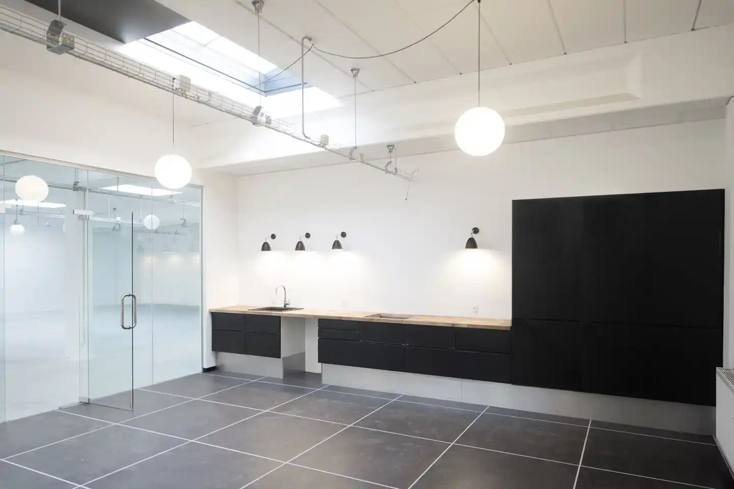 Minimalistisk design med moderne, sort skur, hvid væg, lysekroner, stort glasdøre og skabe og søjler med lys.