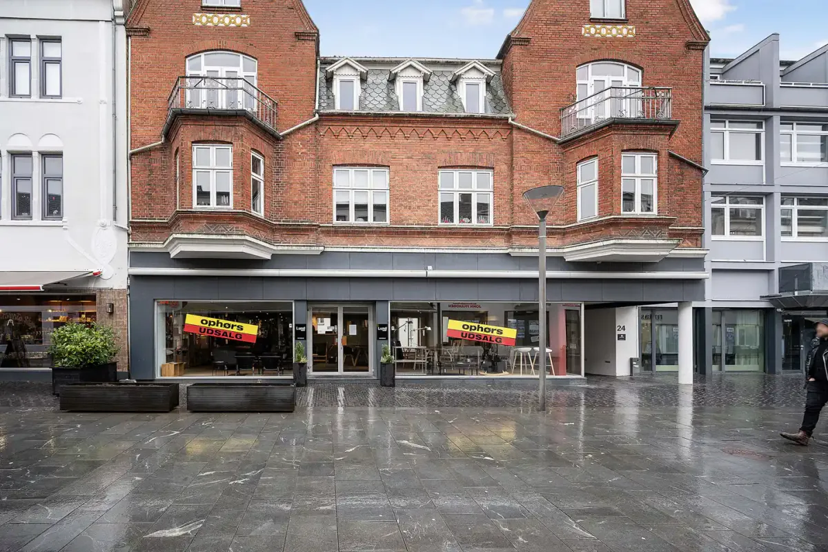 En borger gå ned en tør og blank gade foran en røde murstensbygning med udsalgsskilte i vinduerne