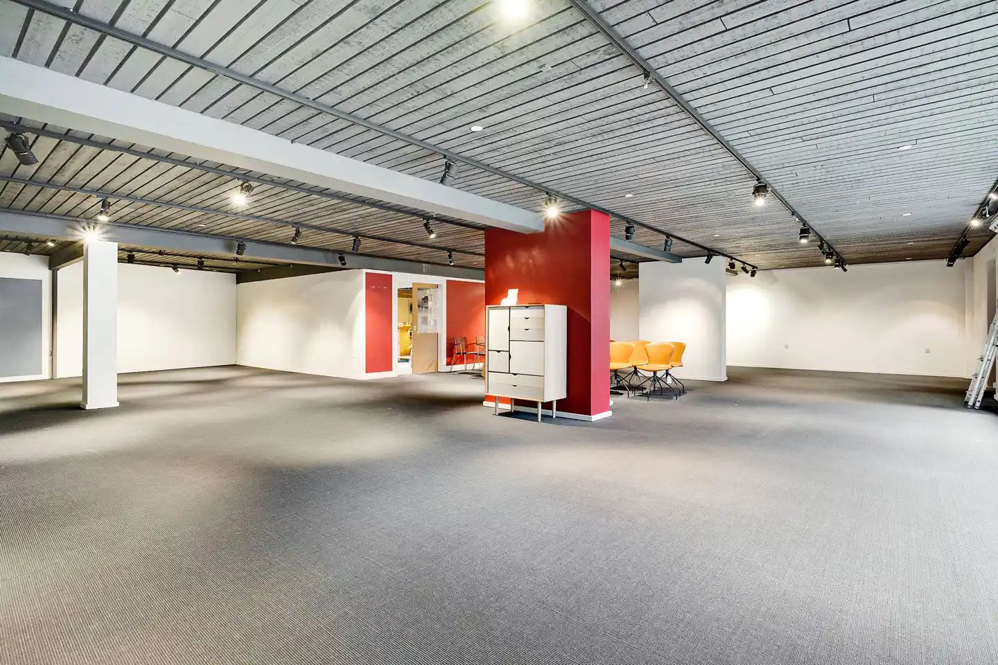 Ledig lokale med loft, vægge og gulv i hvid og rødt og møbler og lysarmatur i gul og rød farve