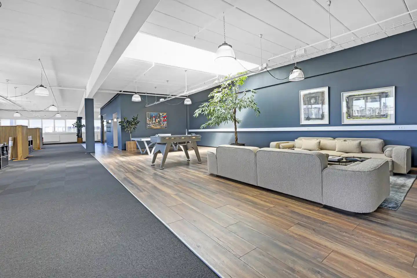 Rummeligt kontorområde med trægulv og moderne møbler, to mødelokaler og et spiseområde med bord og stole