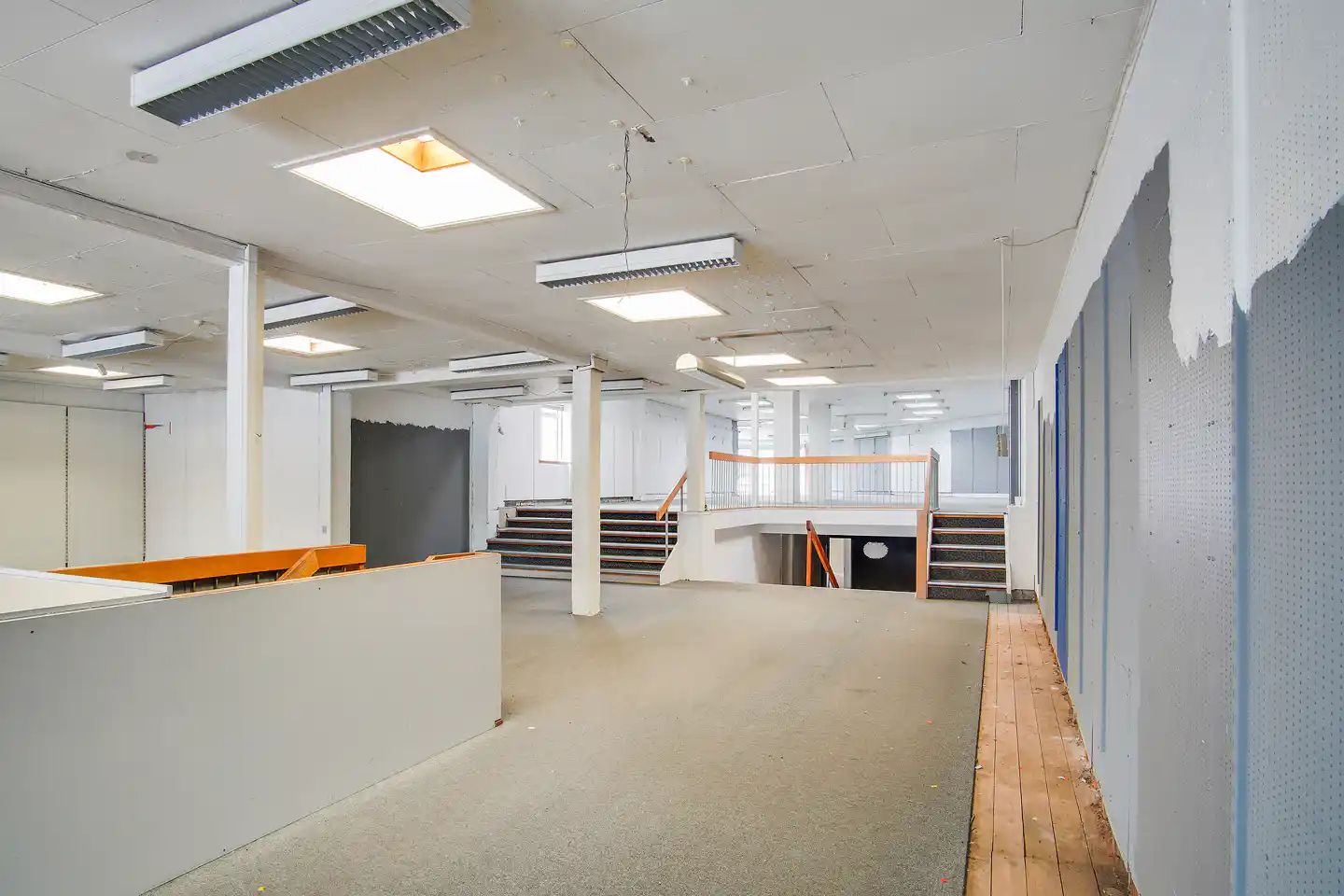 Stort, tømt lokale med højt loft, lysekroner, lyse paneler og tre rækker trin, som fører ned i kælderen