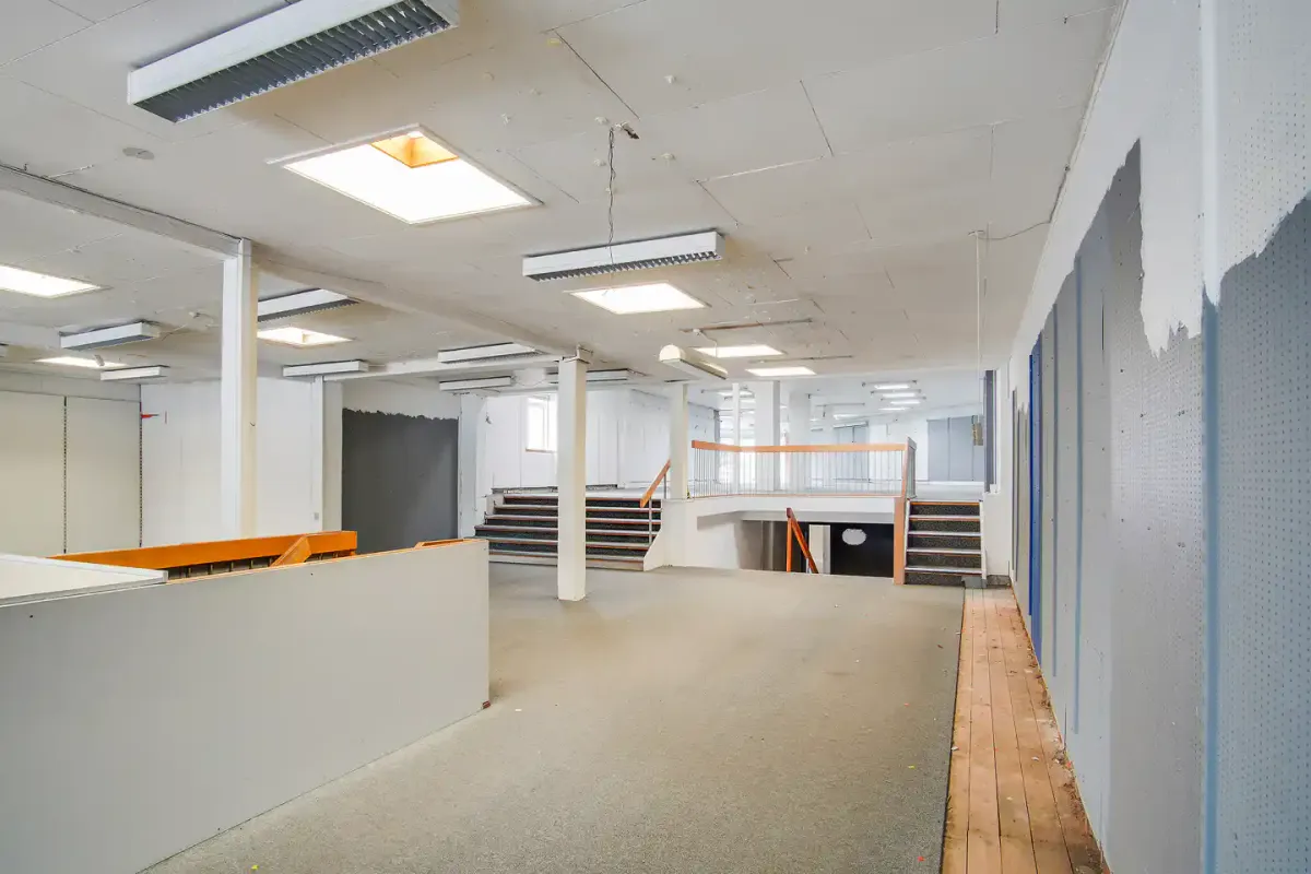 Stort, tømt lokale med højt loft, lysekroner, lyse paneler og tre rækker trin, som fører ned i kælderen