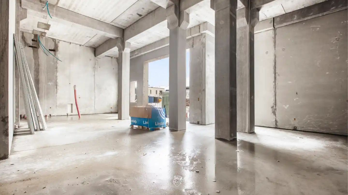 Foto af et tomt lokale i et nyt boligprojekt med betonvægge og gulve