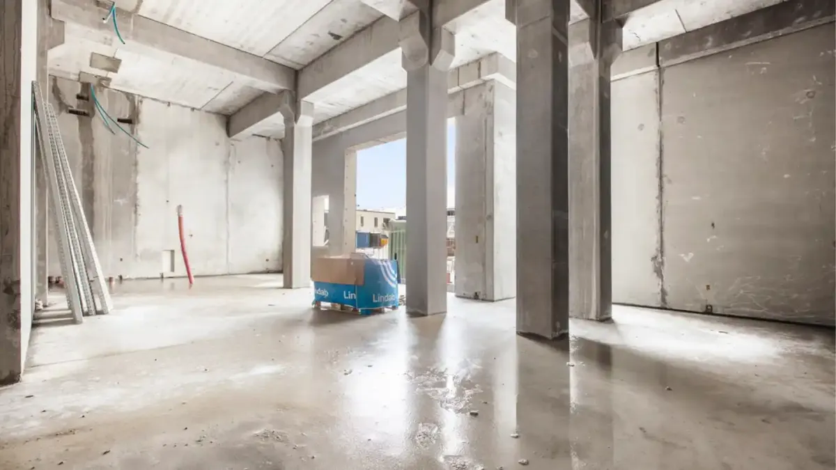 Foto af et tomt lokale i et nyt boligprojekt med betonvægge og gulve