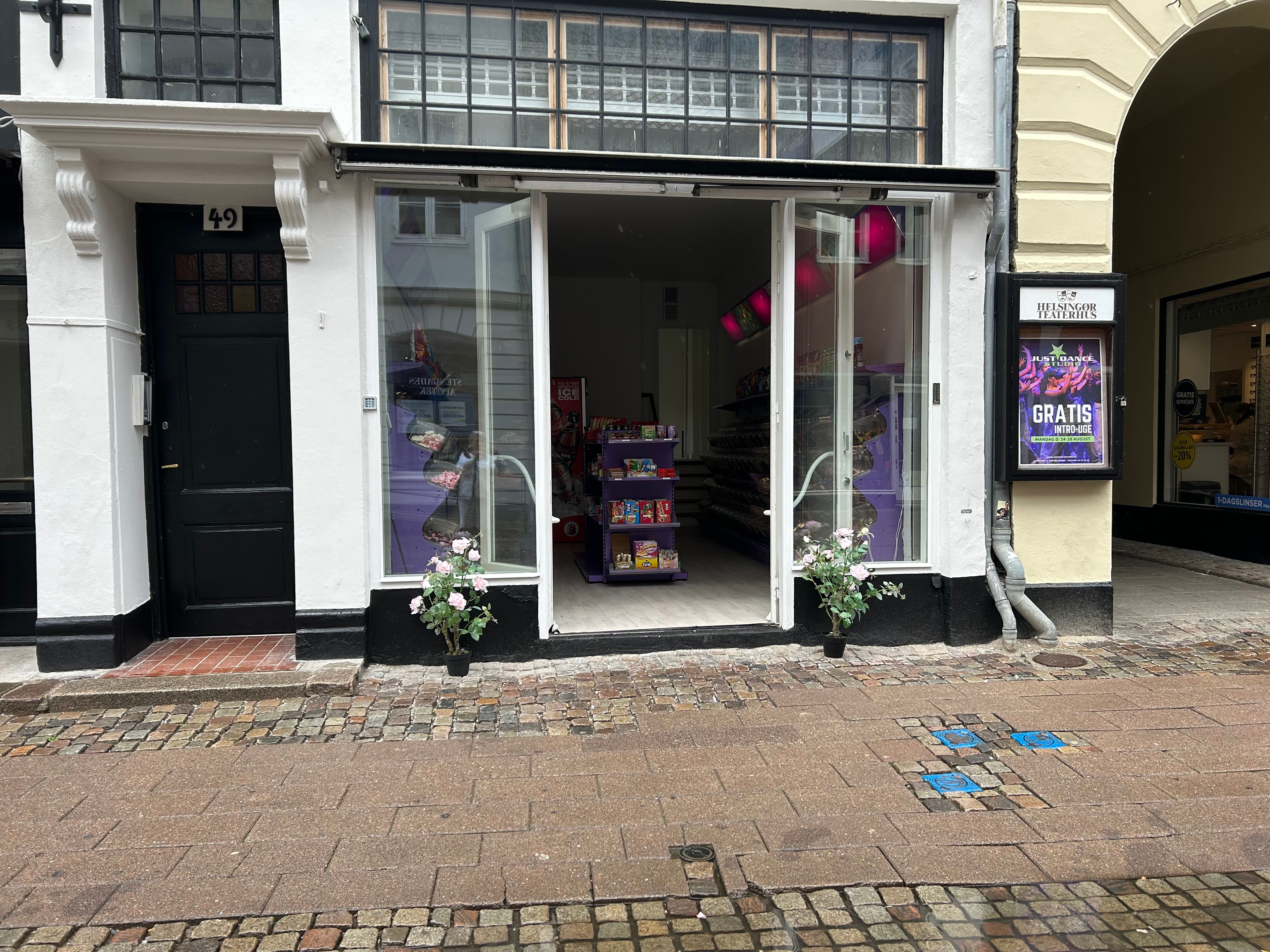 Butik med nummer 49 på Stengade i Helsingør, med åbne glasdøre og lyse farver, samt plantepoteter med blomster udenfor