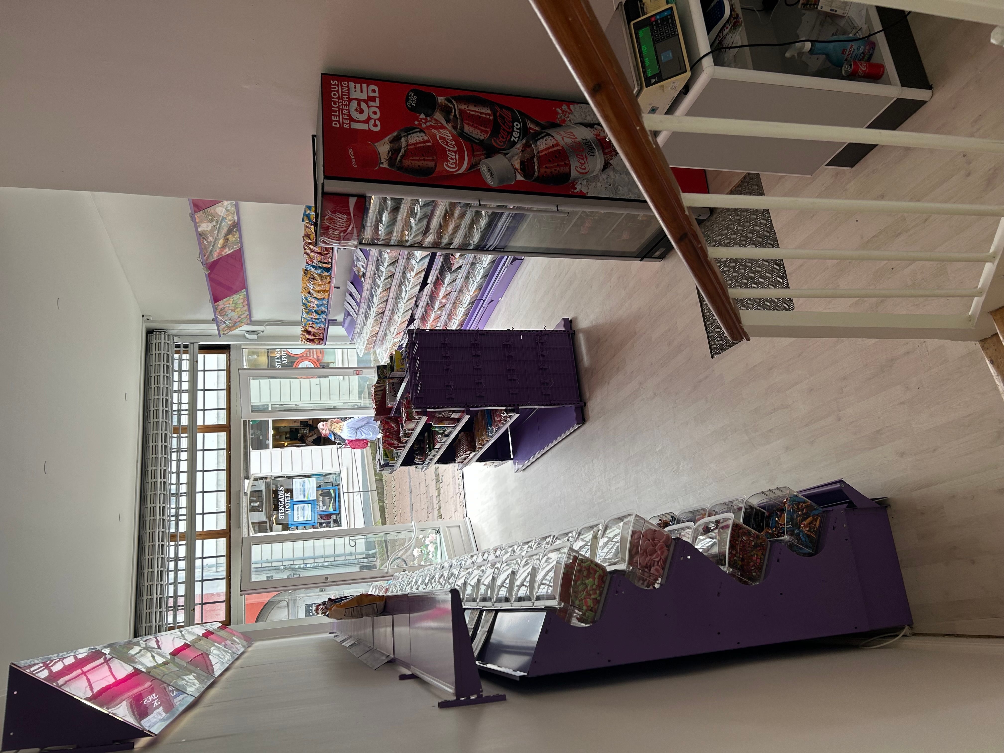 Et vindue med glasruder vender ud mod Stengade. Der er flere butiksreoler med slik og sodavand og en Coca-Cola reklame i
