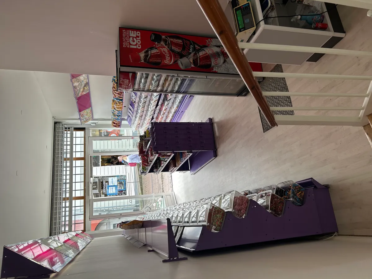 Et vindue med glasruder vender ud mod Stengade. Der er flere butiksreoler med slik og sodavand og en Coca-Cola reklame i