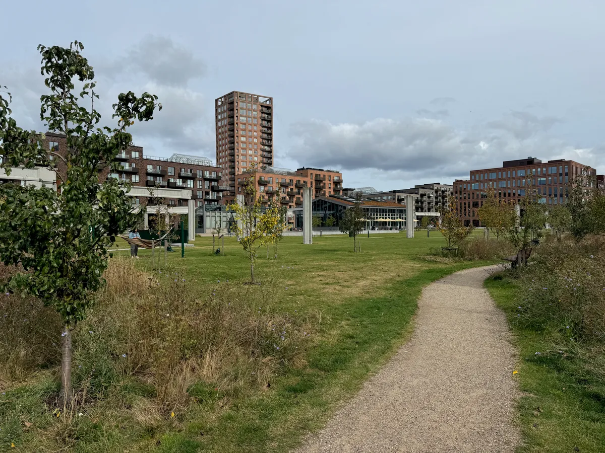 Et grønt område med en sti, træer og buske med en bygning i baggrunden