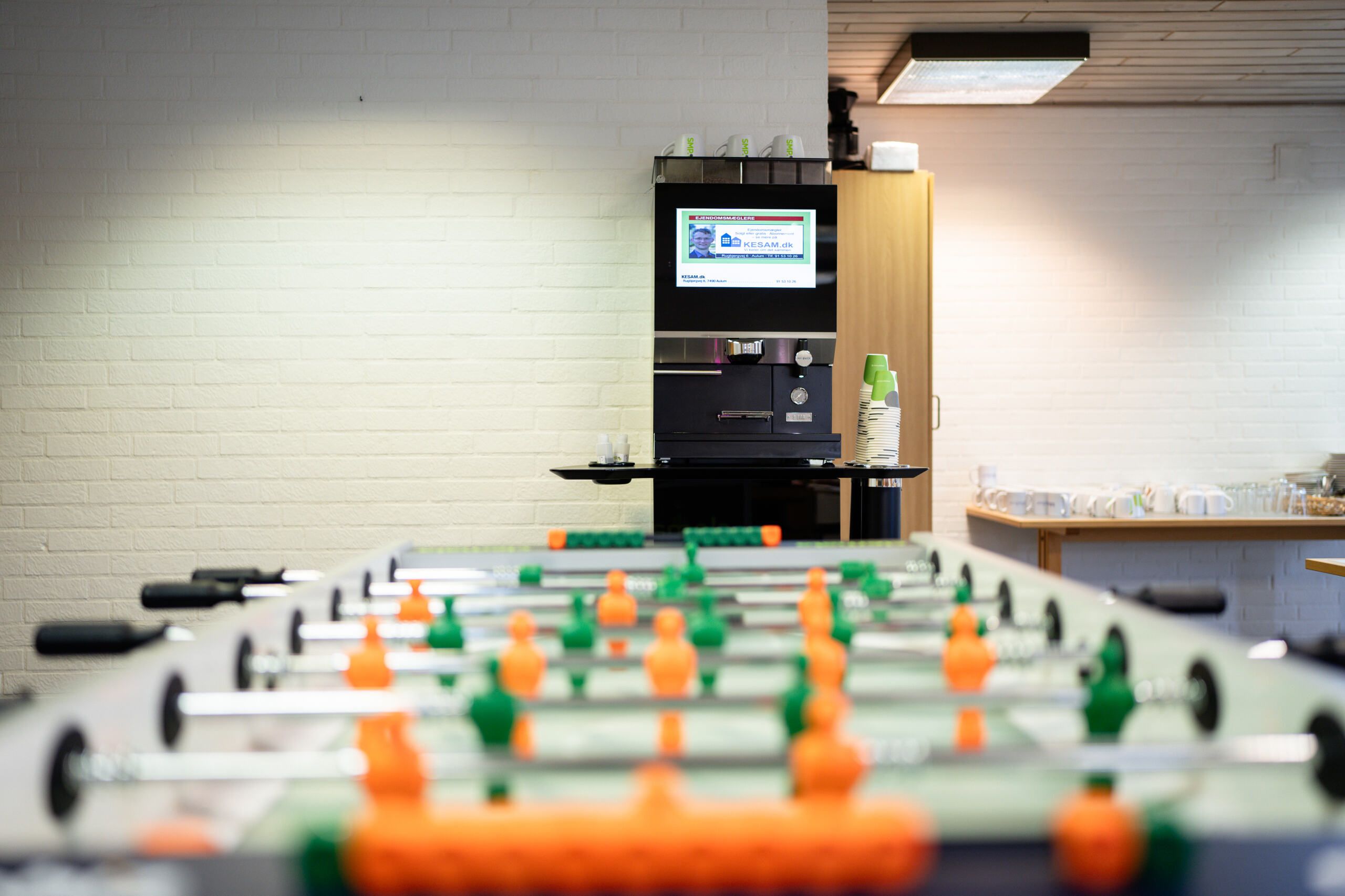 Erhvervsparken Aulums kontorhotel med en foosboldebane, et kaffemaskine og en tv-skærm, hvor der vises en reklame