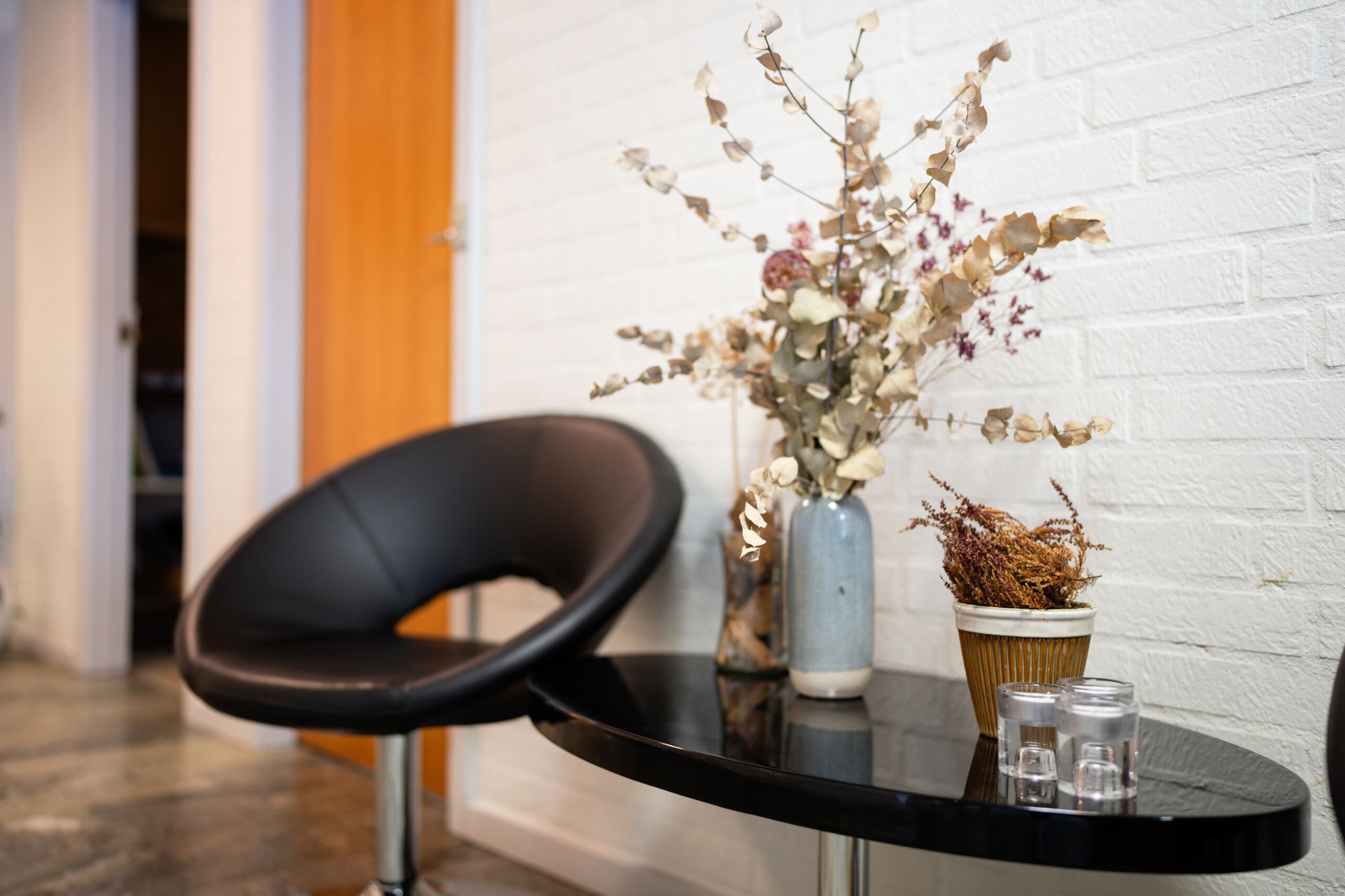 Sort stol med høj stolsæde står i spidsen af bord med glaskugler og to plantepotter med tørret grønt og brun bladverk