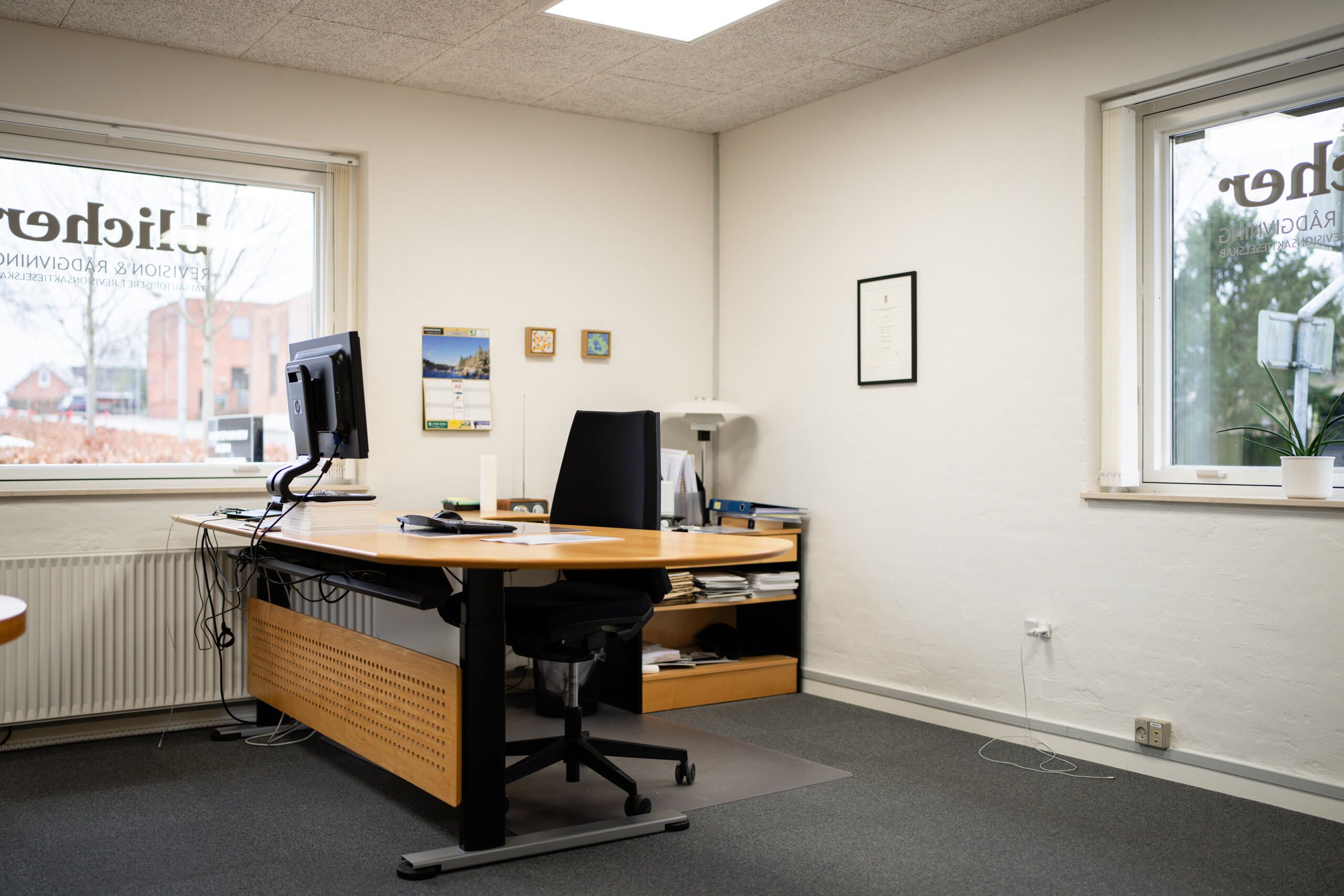 Et tomt kontor med skrivebord, stol, plante og fire vinduer, der er mærkede med tekst og billeder