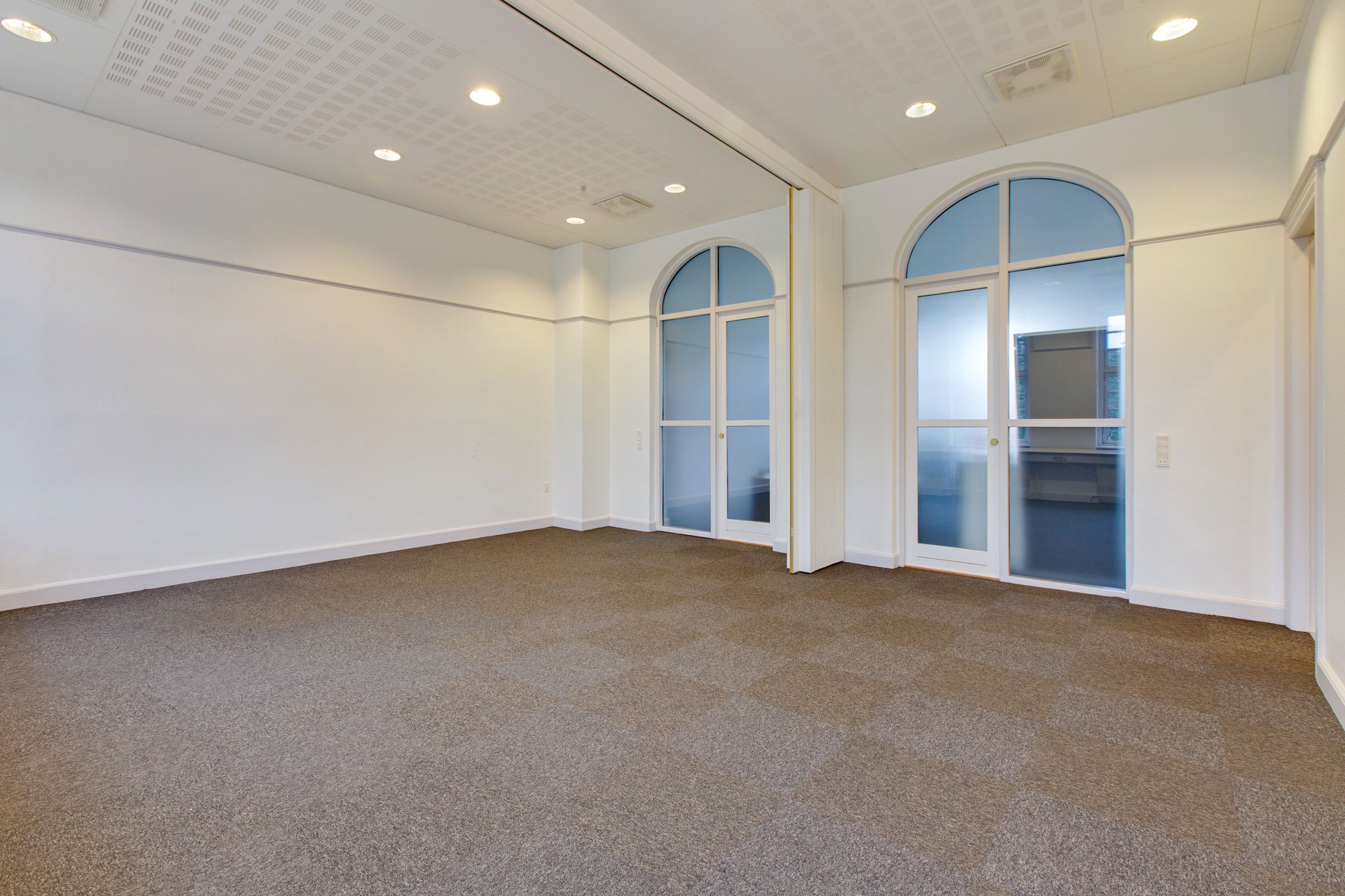 Lys og ren møderum med hvidt loft, hvide vægge og lysegrå gulvbelægning, to glasdøre og gulve med mønstret udformet som