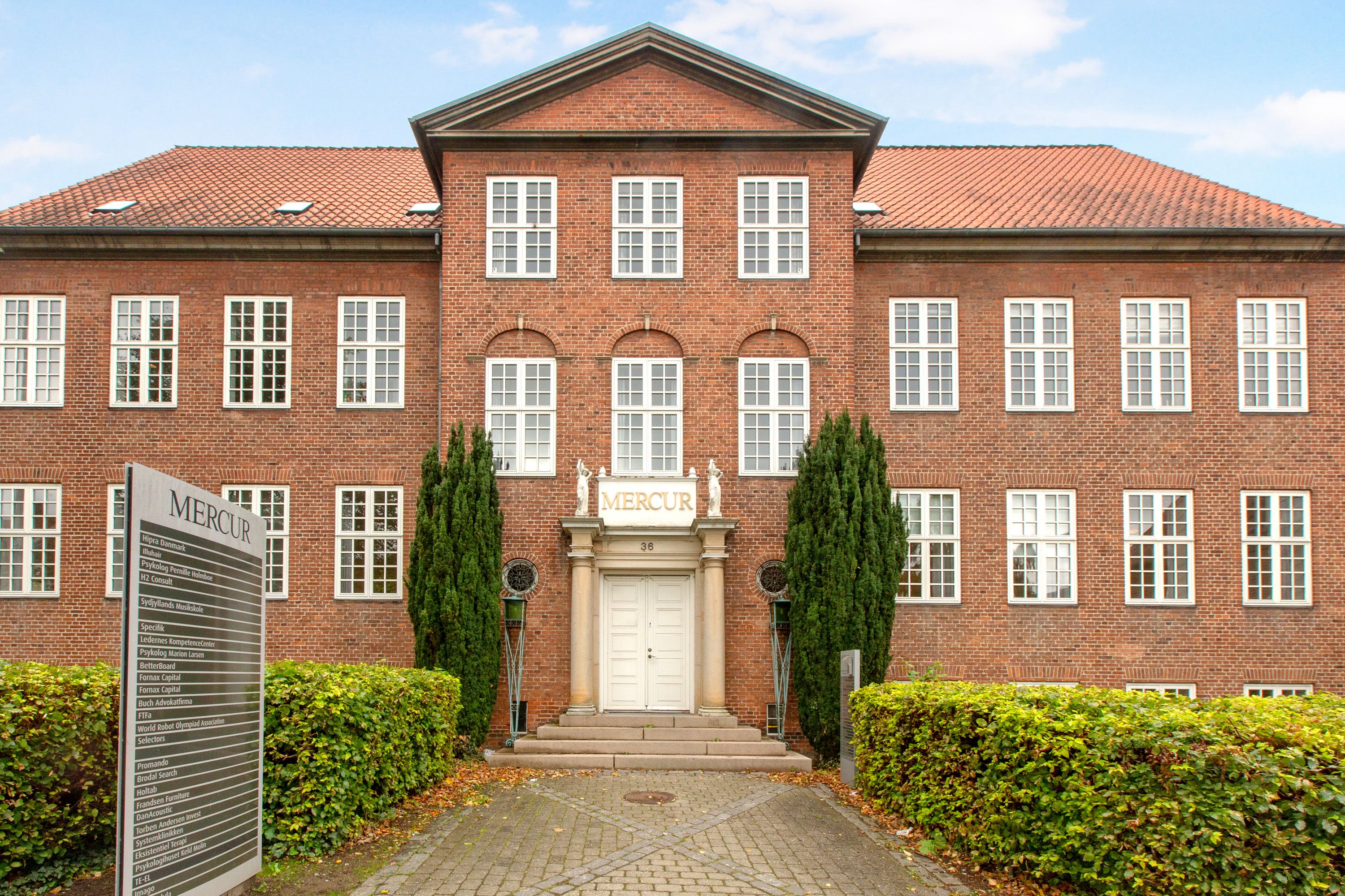 MERCUR bygning med rød mursten og hvide vindueskarme, mærkeplade med tekst og statuer på tagkanten