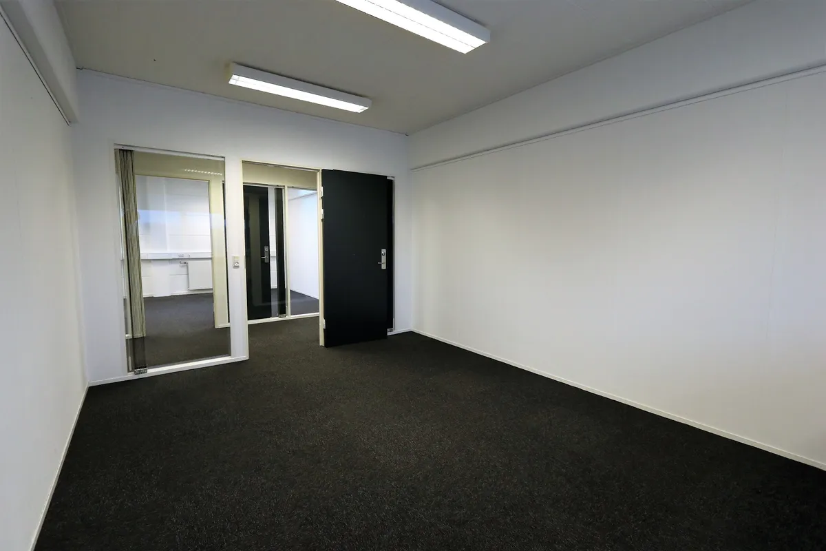 Lukket og indflytningsklart kontorlokale med glasdøre og sort trægulv. Væggene er hvide og der er en lysekron på loftet.