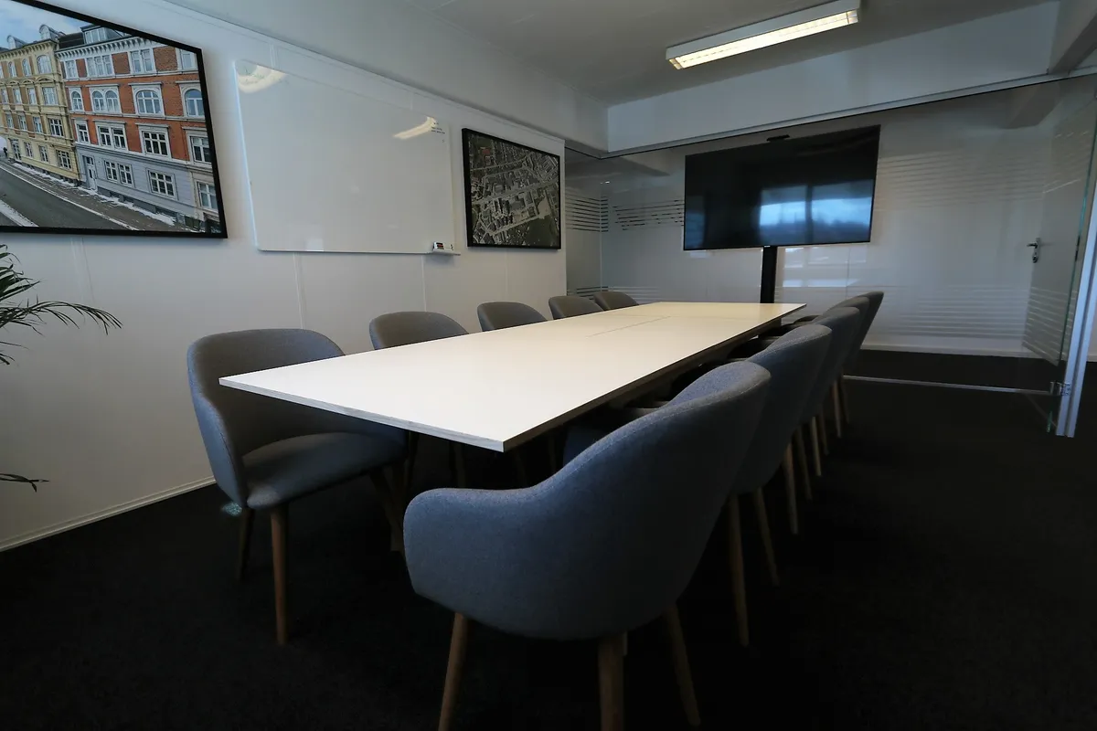 Kontorlokale med lyse vægge og gulvvedligeholdelse, samt skrivebord og flere sæder.