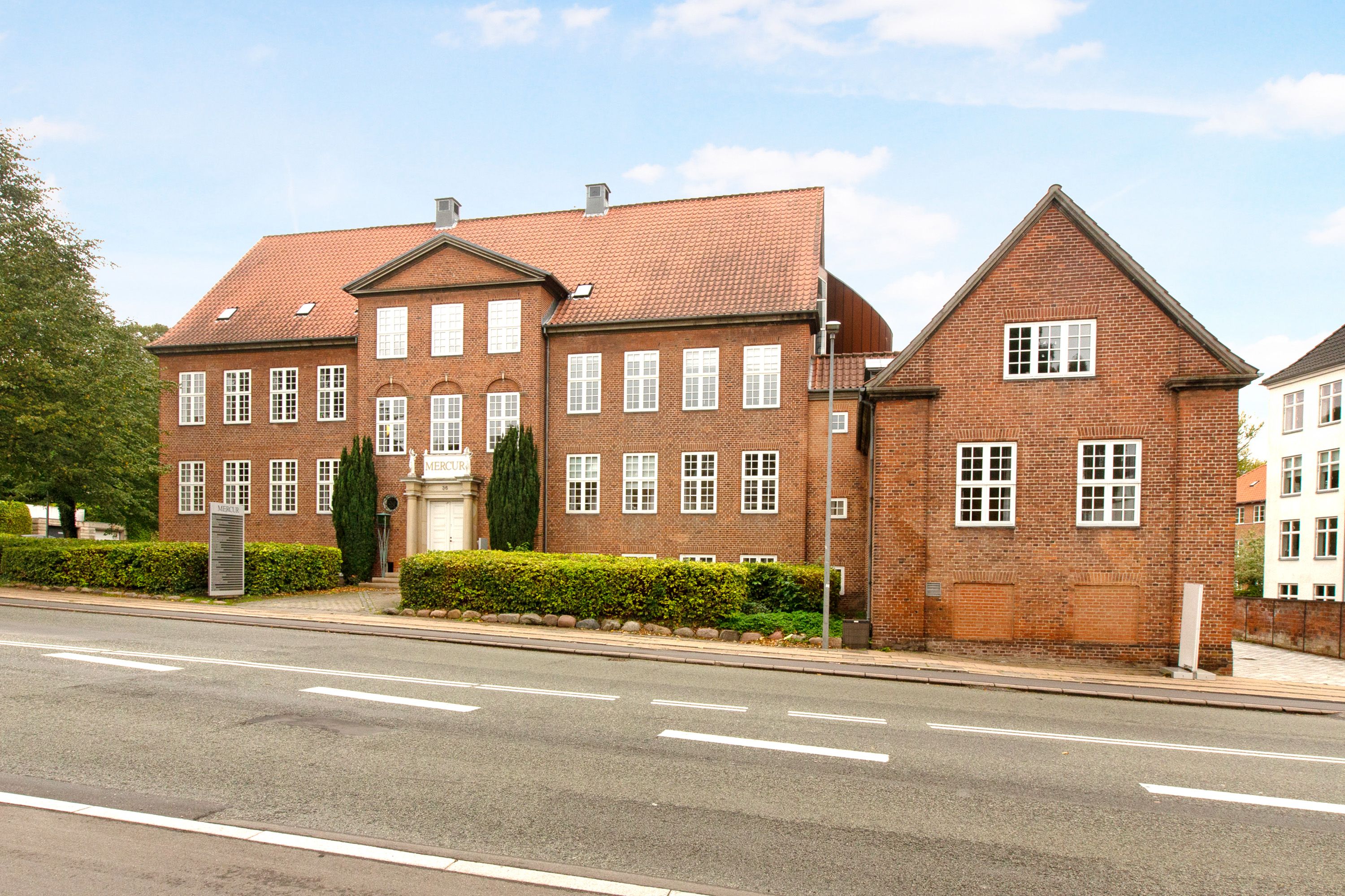 En stor rødmaursten bygning med flere vinduer og et skilt med teksten MERCUR i facaden