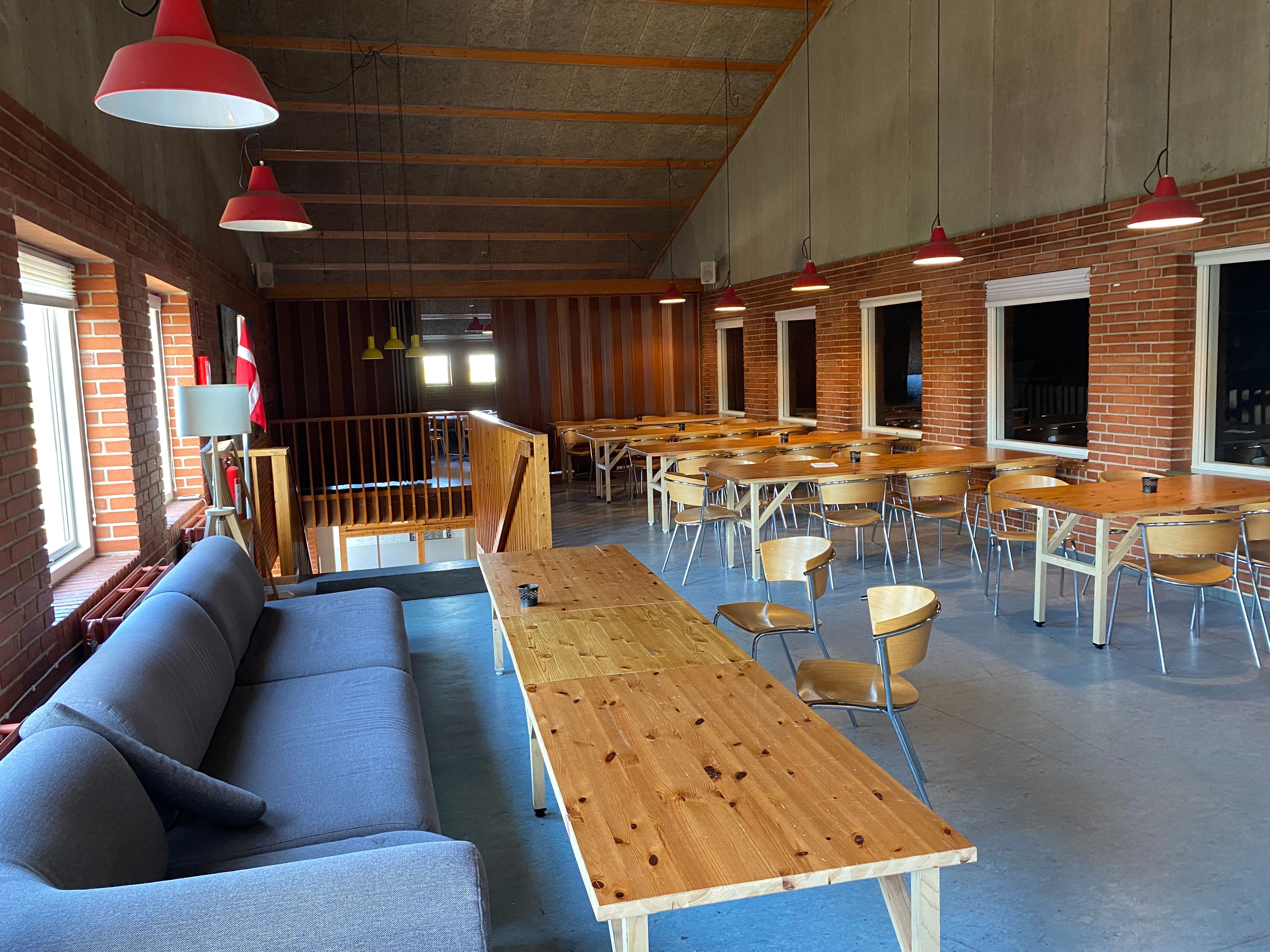 Elegant køkken og spisesal med lyse loftslamper og træborde og stole samt sofa og terrasse med flag.