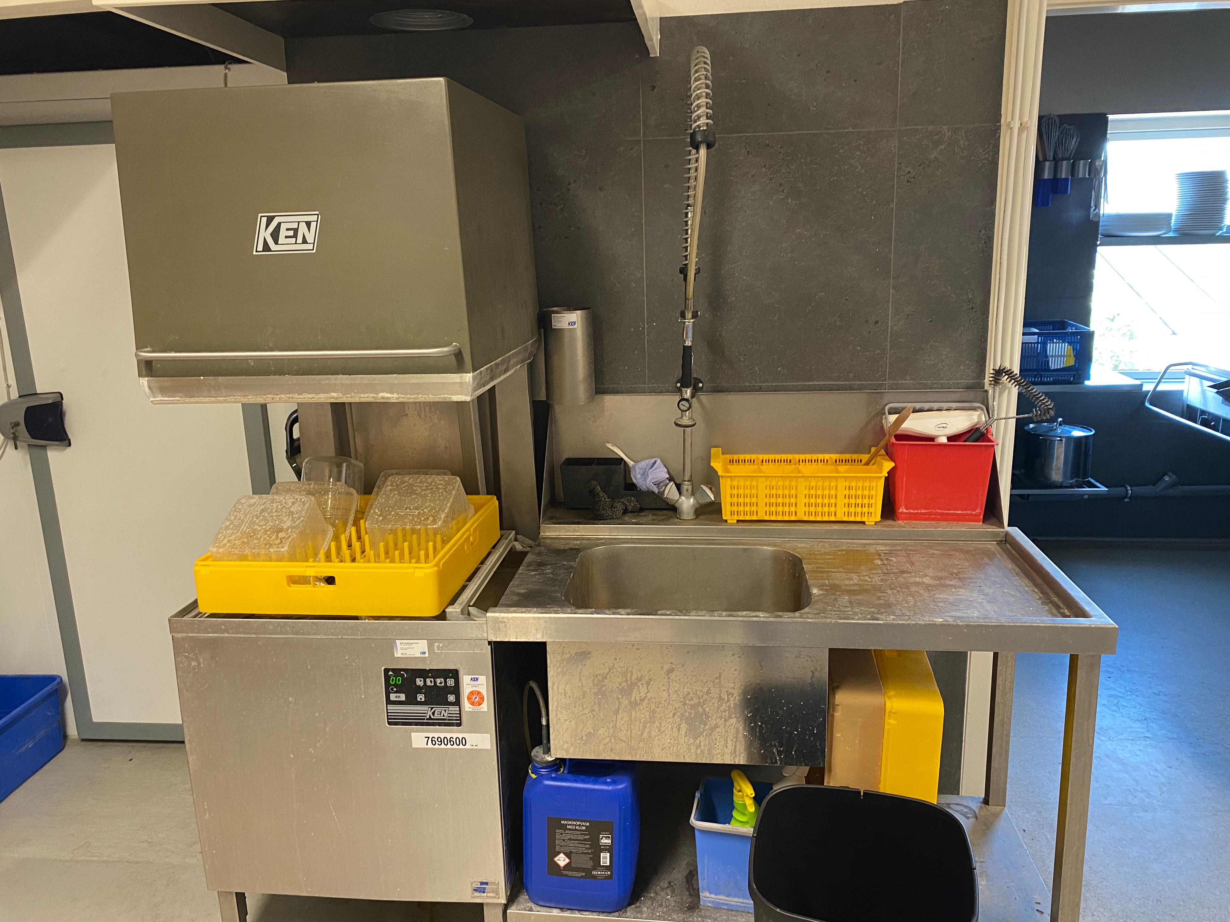 Moderne produktionskøkken med rensningsmaskine, vaskebækken og forskellige opbevaringsbøsser og -kurve til glas og