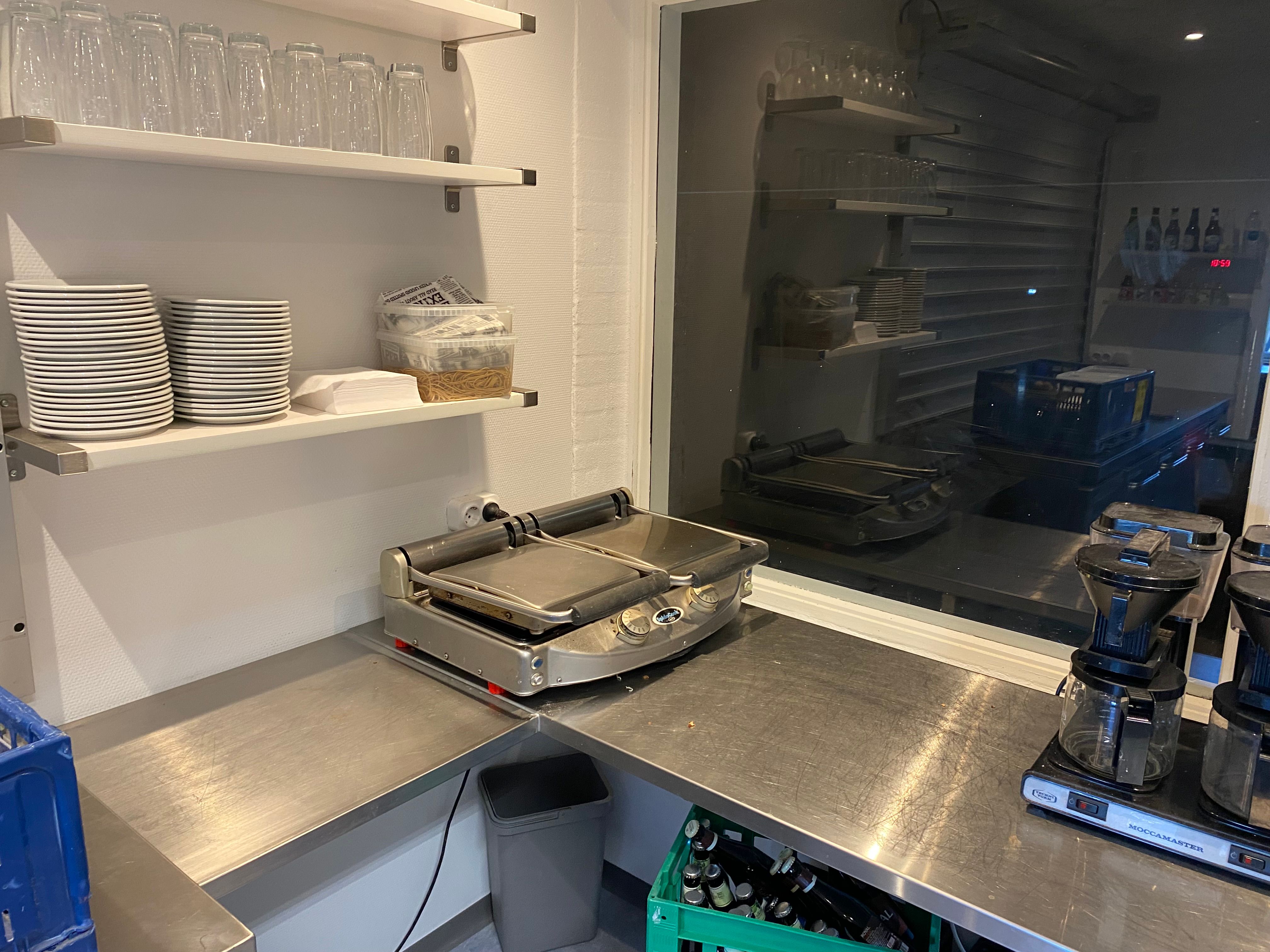 Indkøbsvogne og mopedcykel i et produktionskøkken med en sandeltræbrædder og en grydeplade samt et kaffemaskine