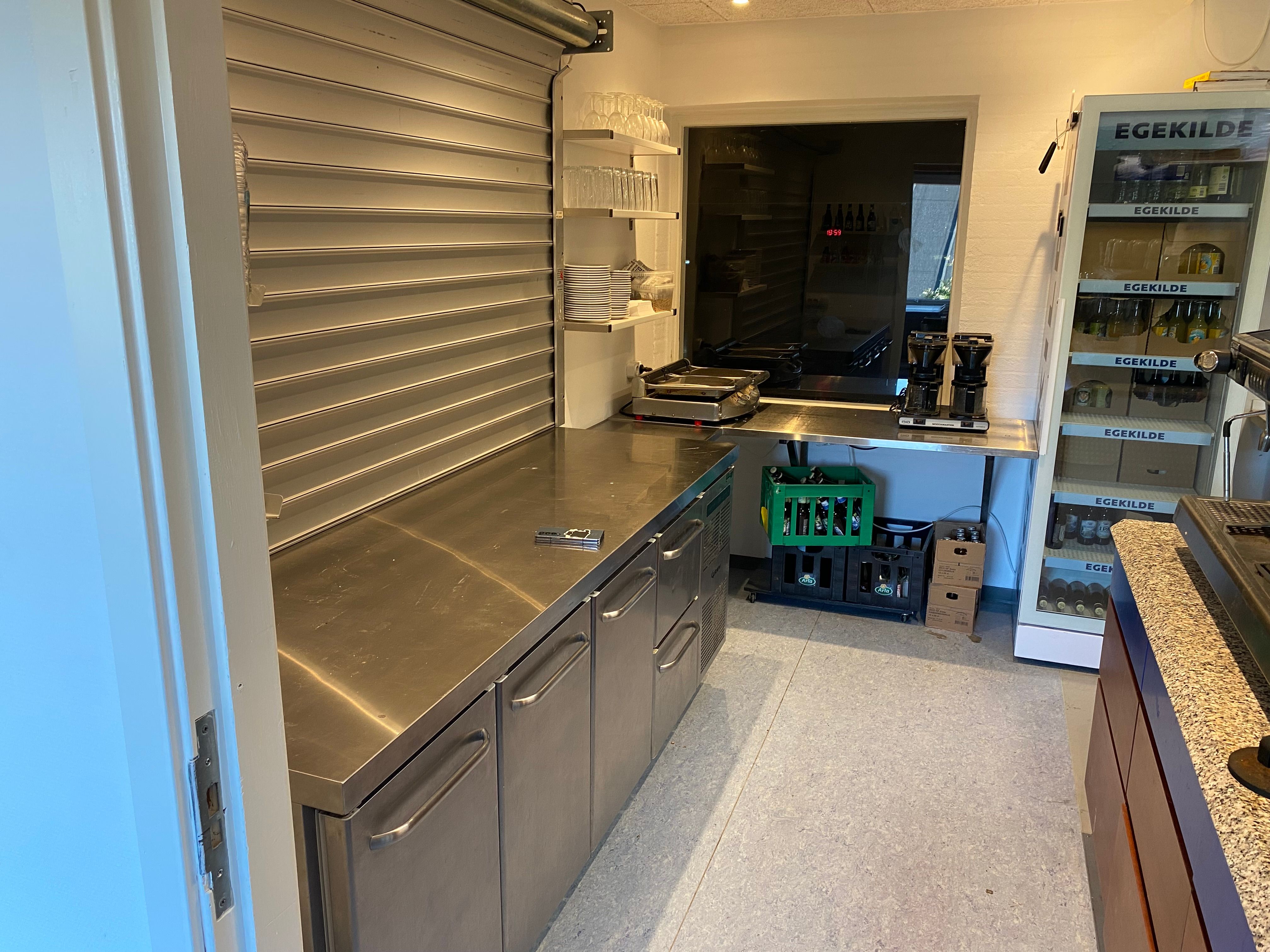Moderne køkken med flere køleskabe, indretning til catering, salg og take-away. Her er der en kaffemaskine, gryder og