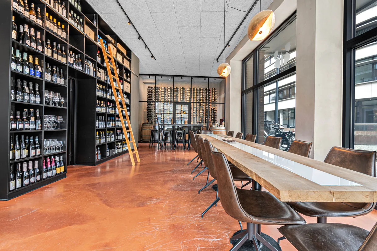 En stor, åben område med borde og stole samt vinflasker i rækker og et vinkælder med tønder i baggrunden