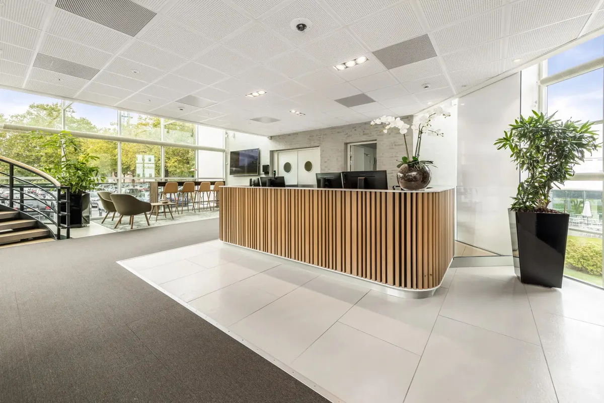 Moderne lobby med hvide vægge og træpaneler, hvidt gulv og gulvbelægning, lyse glasvinduer og plantepotter, og et bord med