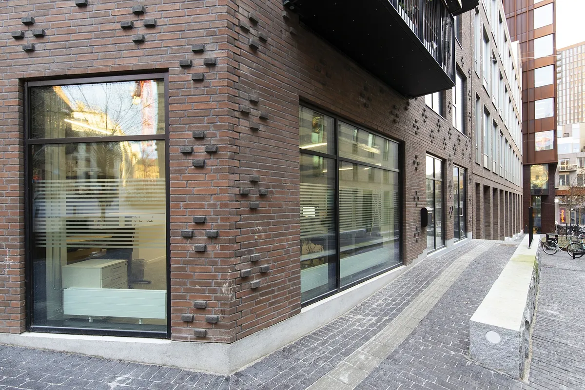 En ny bygning med glasruder og mursten. En række kontorer og et parkerede cykler langs gaden. Et skarpt og funktionelt