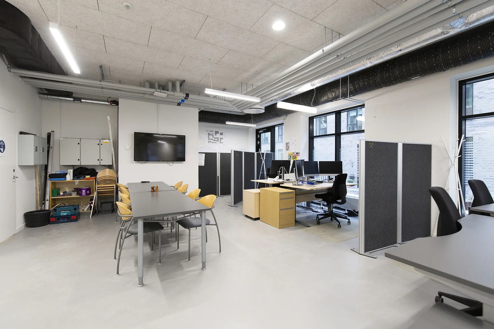 Moderne kontor med lyse lofter, lysekroner, skriveborde, stole, skærme og opbevaringsskabe.