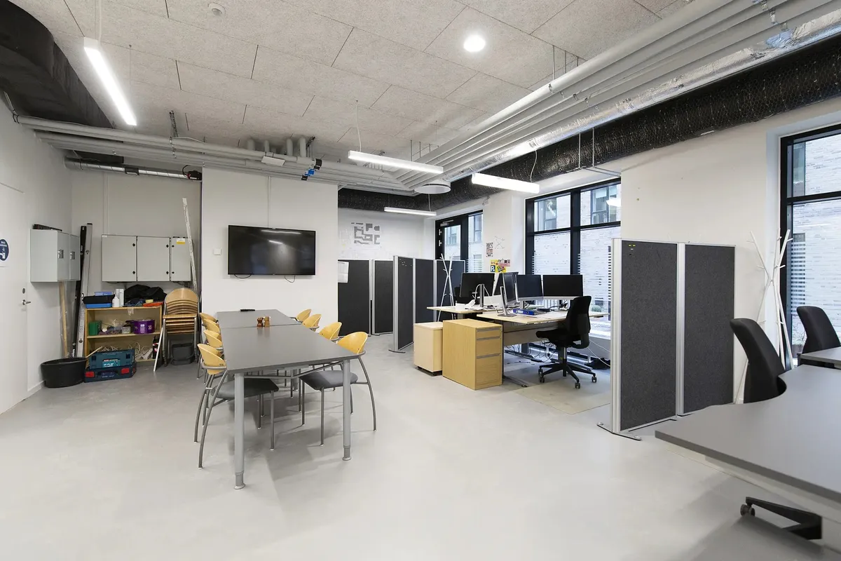 Moderne kontor med lyse lofter, lysekroner, skriveborde, stole, skærme og opbevaringsskabe.