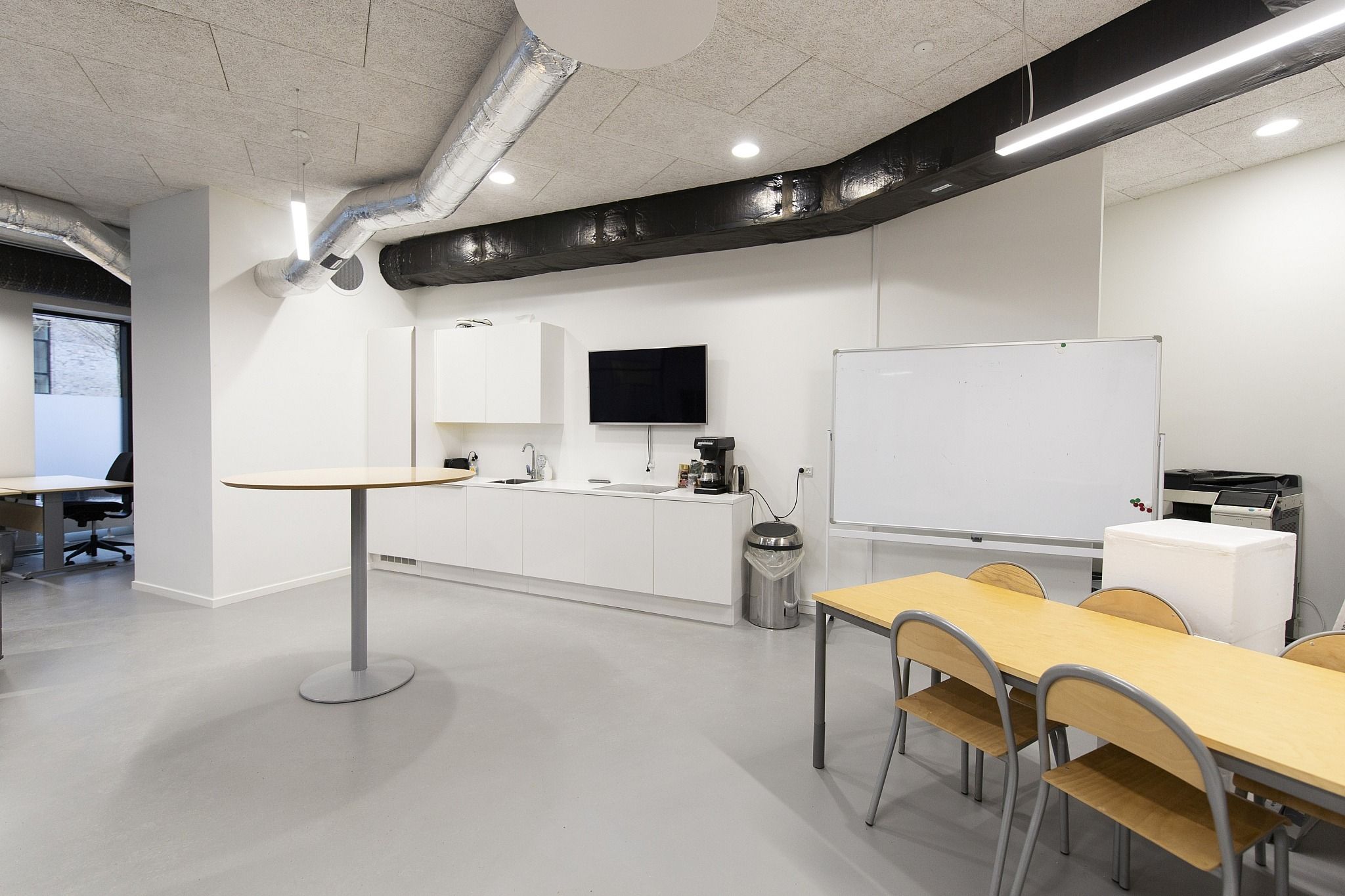 Moderne kontor med højloft, runde borde, hvide vægge, hvide skabe og en stor whiteboard