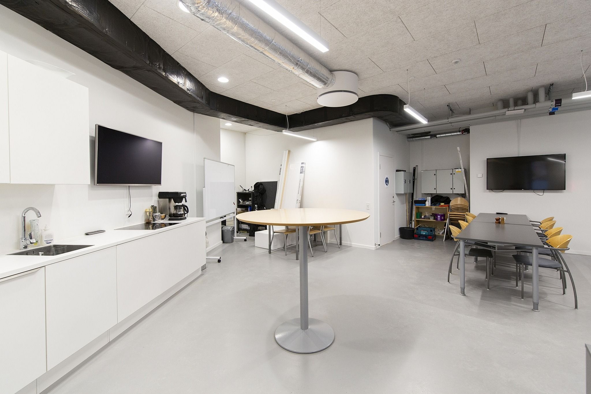 Et højloftet kontor med moderne møbler og teknologi, høje lofter, køkken med lyserøde apparater og flere skriveborde