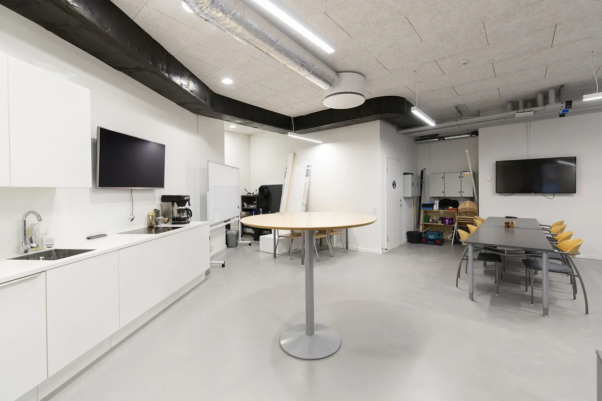 Et højloftet kontor med moderne møbler og teknologi, høje lofter, køkken med lyserøde apparater og flere skriveborde