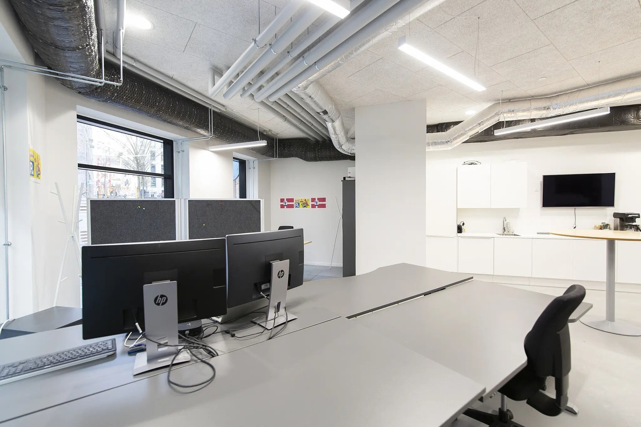 Kontor med højloft, lyse plafonds, to skriveborde med computere og tavler samt lyse loftsventilatorer