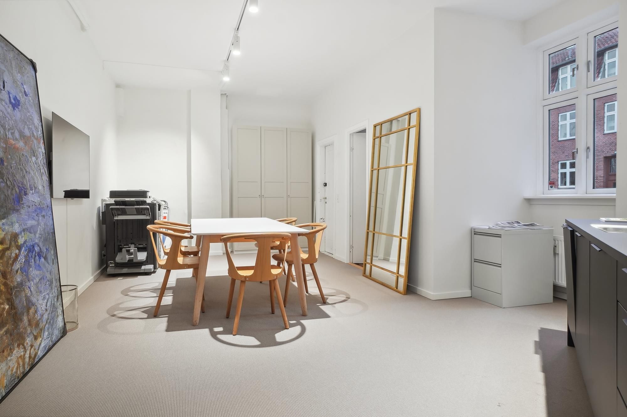 En minimalistisk mødelokale med hvide vægge og lysegul gulvbelægning samt en stor kunstværk mod væggen og en hvid borde og