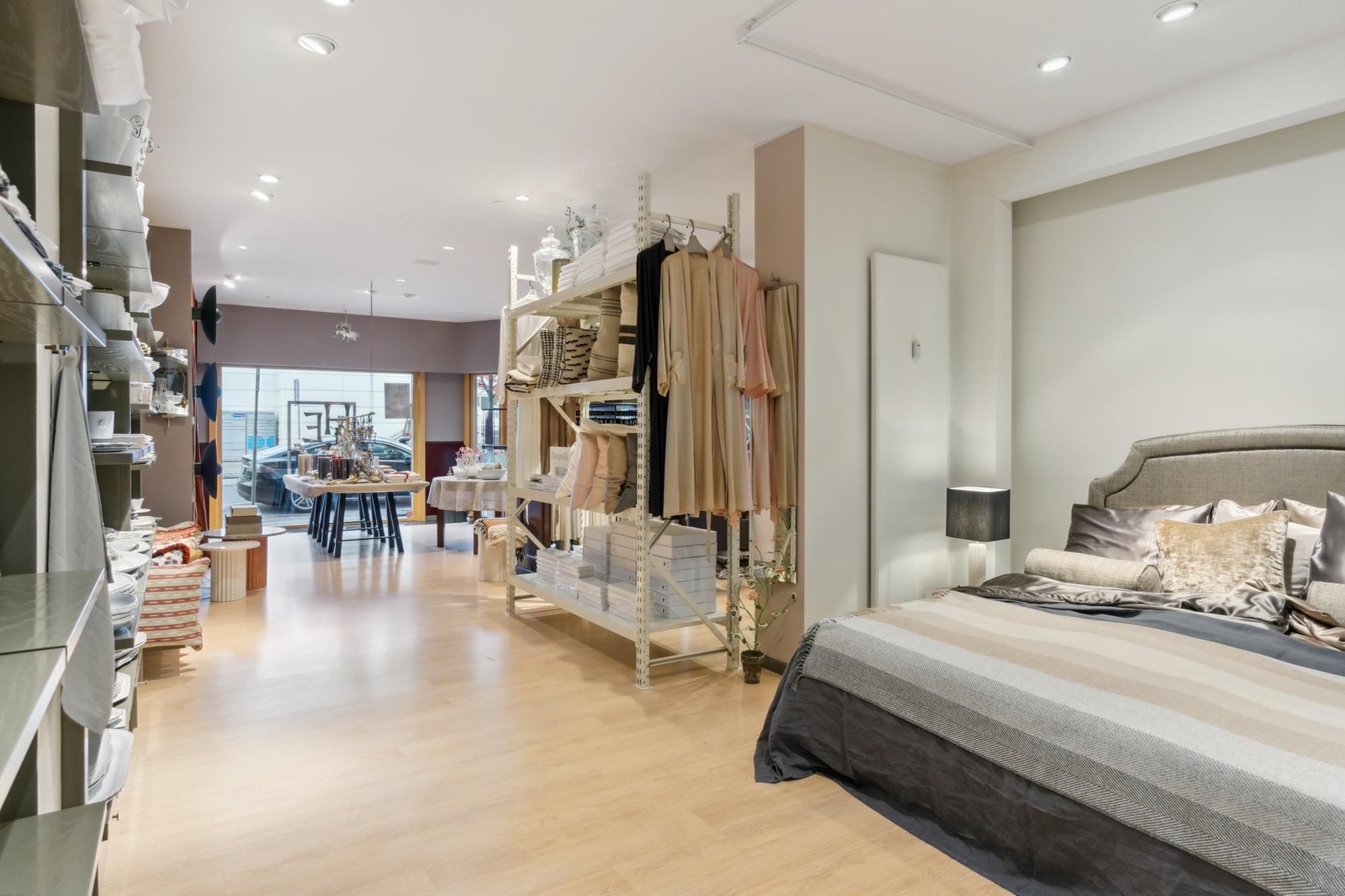 Det store lokale med møbler og tøj, samt store vinduer med udsigt til parkerede biler