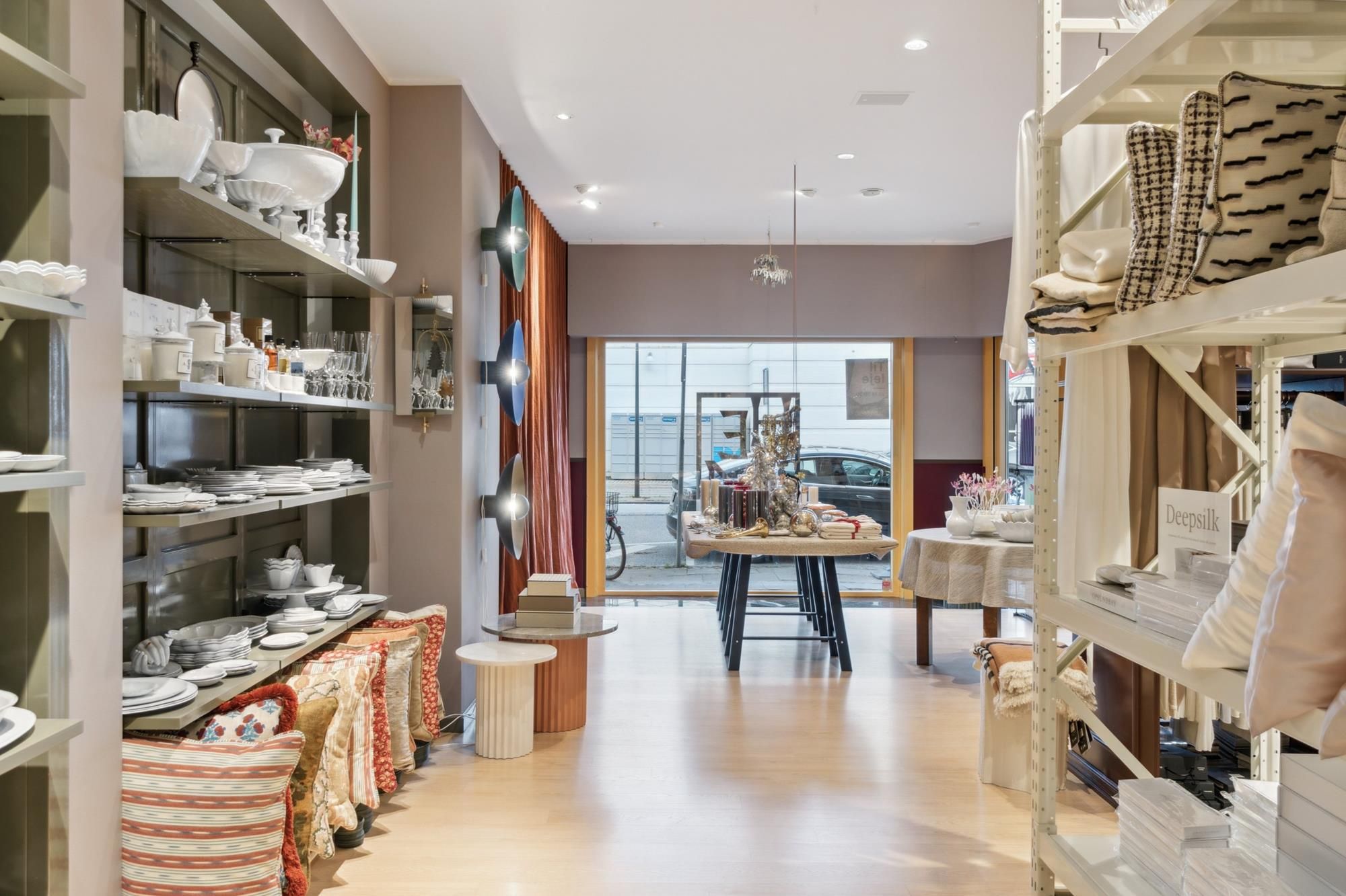 Indretning med lyse vægge, høje hylder med glas og porcelæn, lyse gulvvedlige og lysekroner, møbler og tæpper, udendørs