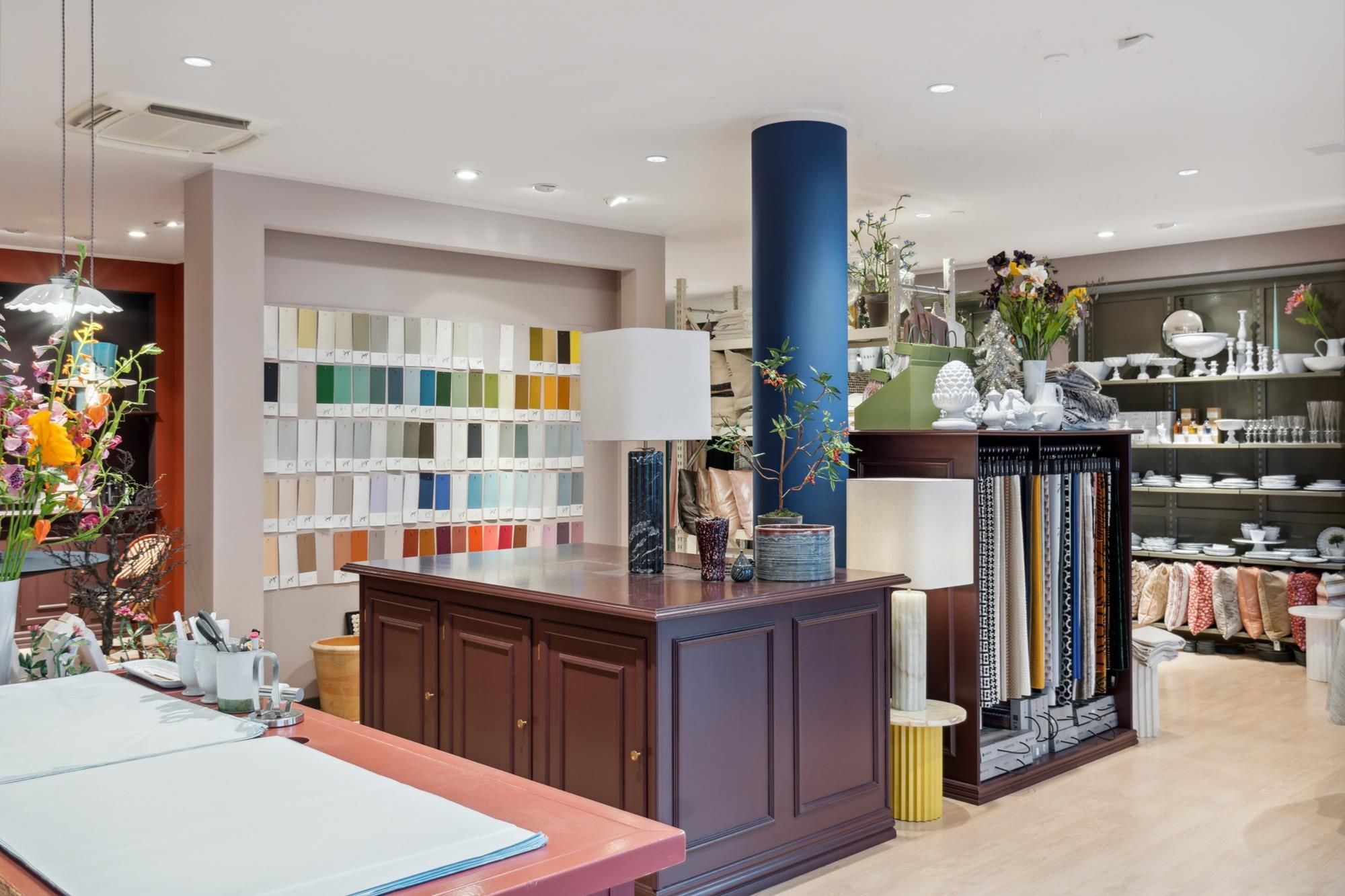Lyst og moderne detaillejemål med mange farveprøver, blomster, møbler, lysekroner og eksemplarer af møbler og tæpper.
