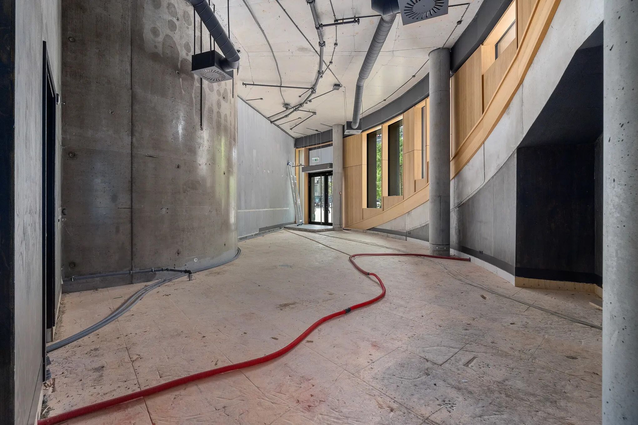 Betonsøjler og hvide loftsrør i en nybygget lejlighed med rød slange og træpaneler