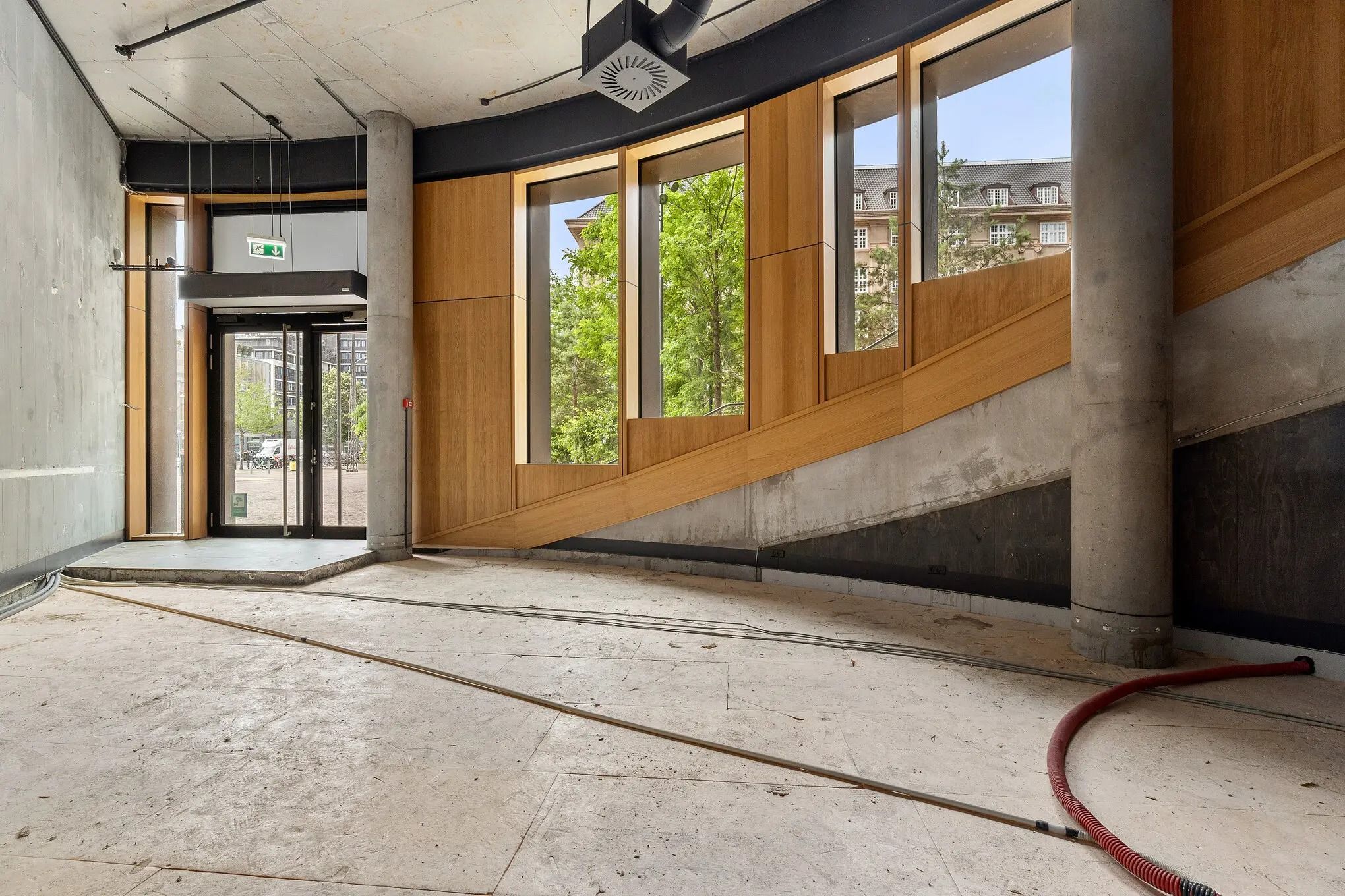 Dobbeltglasdør og vinduer i en møbleret indgangshal med lyse gulve og rødt slangemateriale